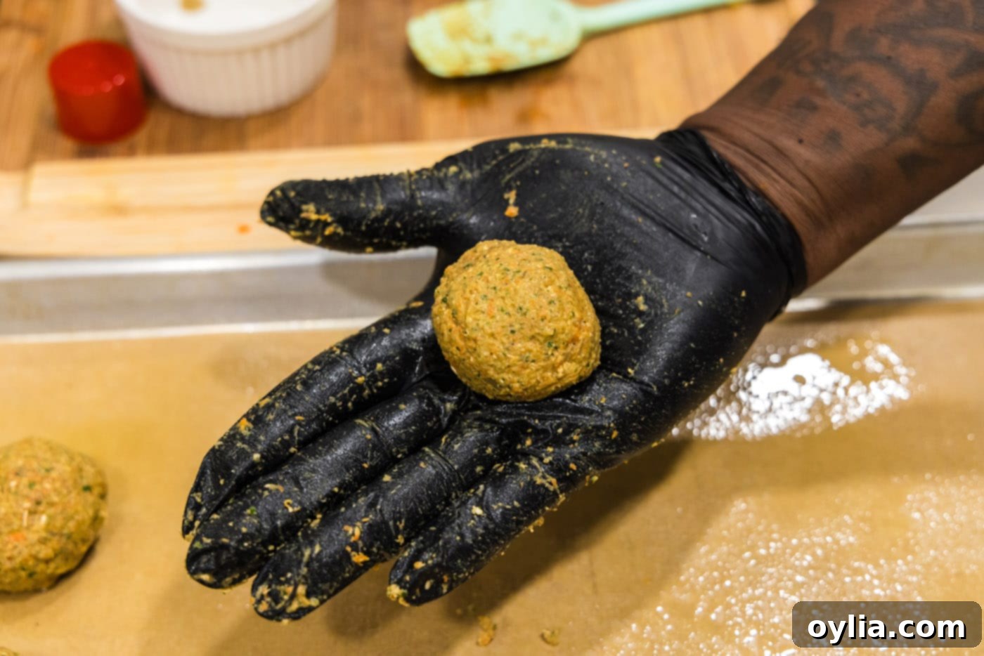 A hand holding a perfectly rolled lentil meatball.