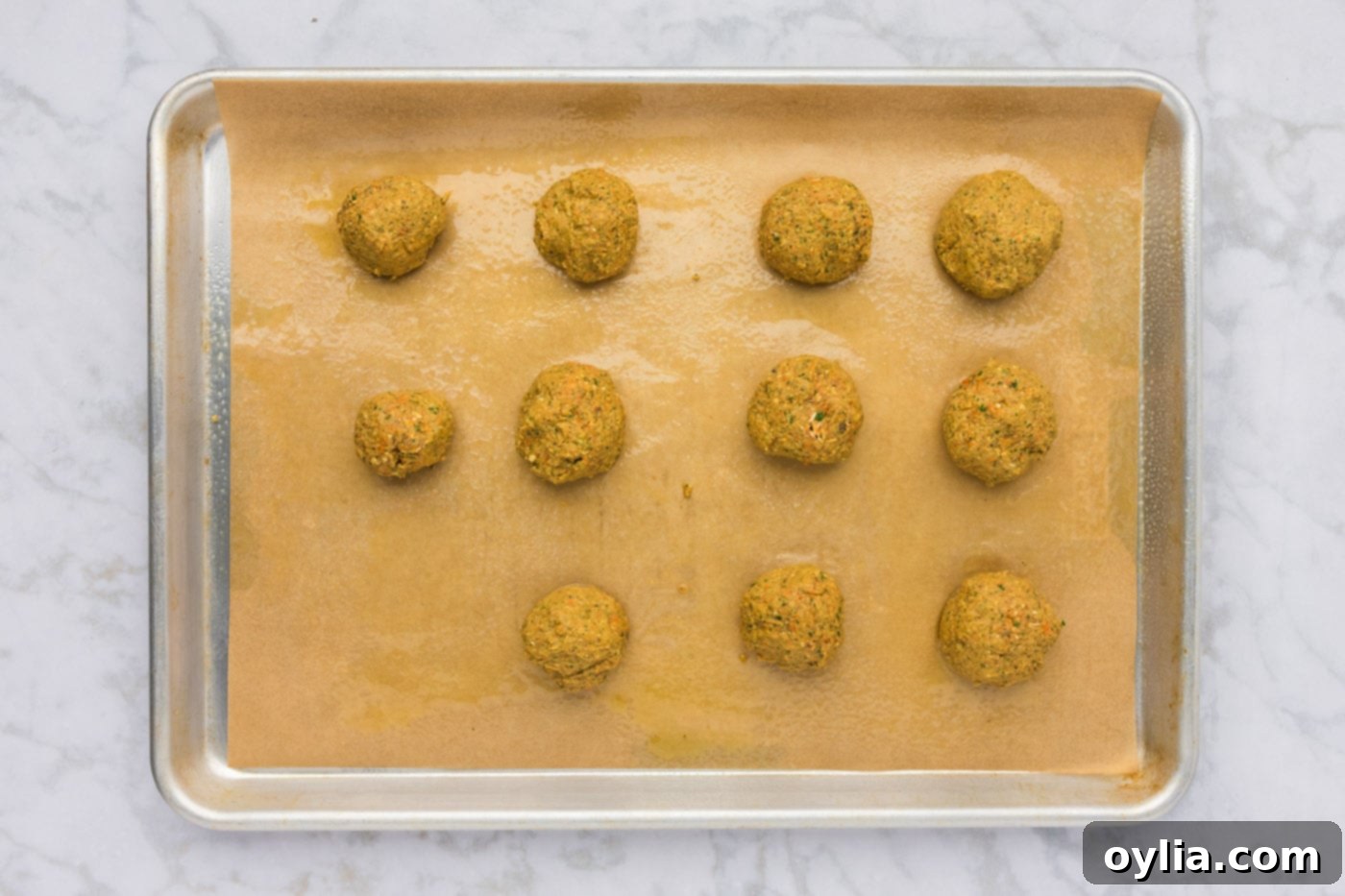 Several rolled lentil meatball dough portions are arranged on a parchment-lined baking sheet, ready for baking.