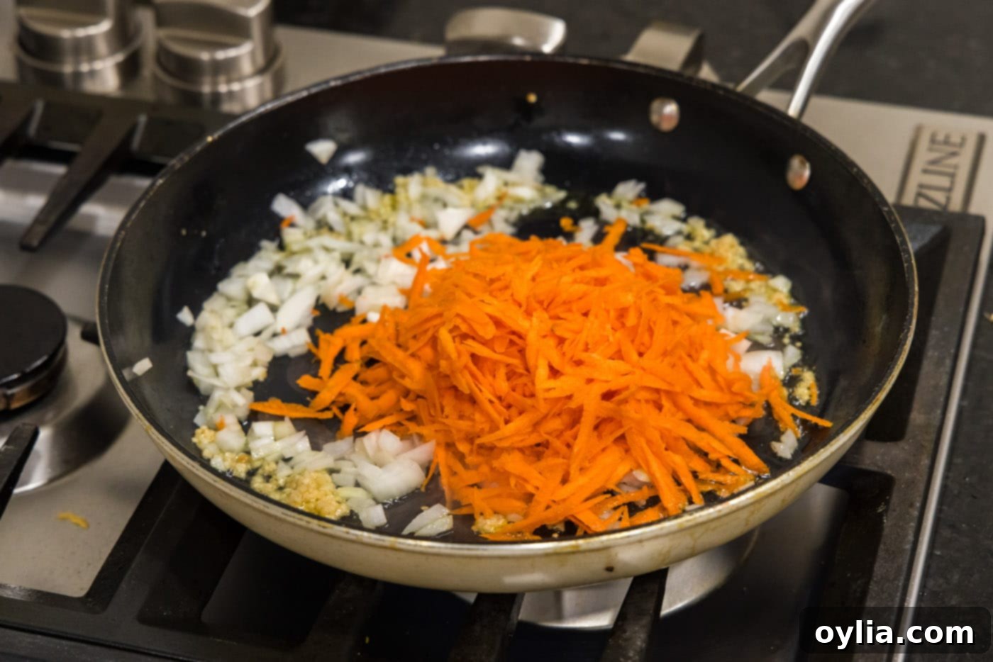 Minced garlic, chopped onion, and shredded carrot are added to a hot skillet with olive oil.