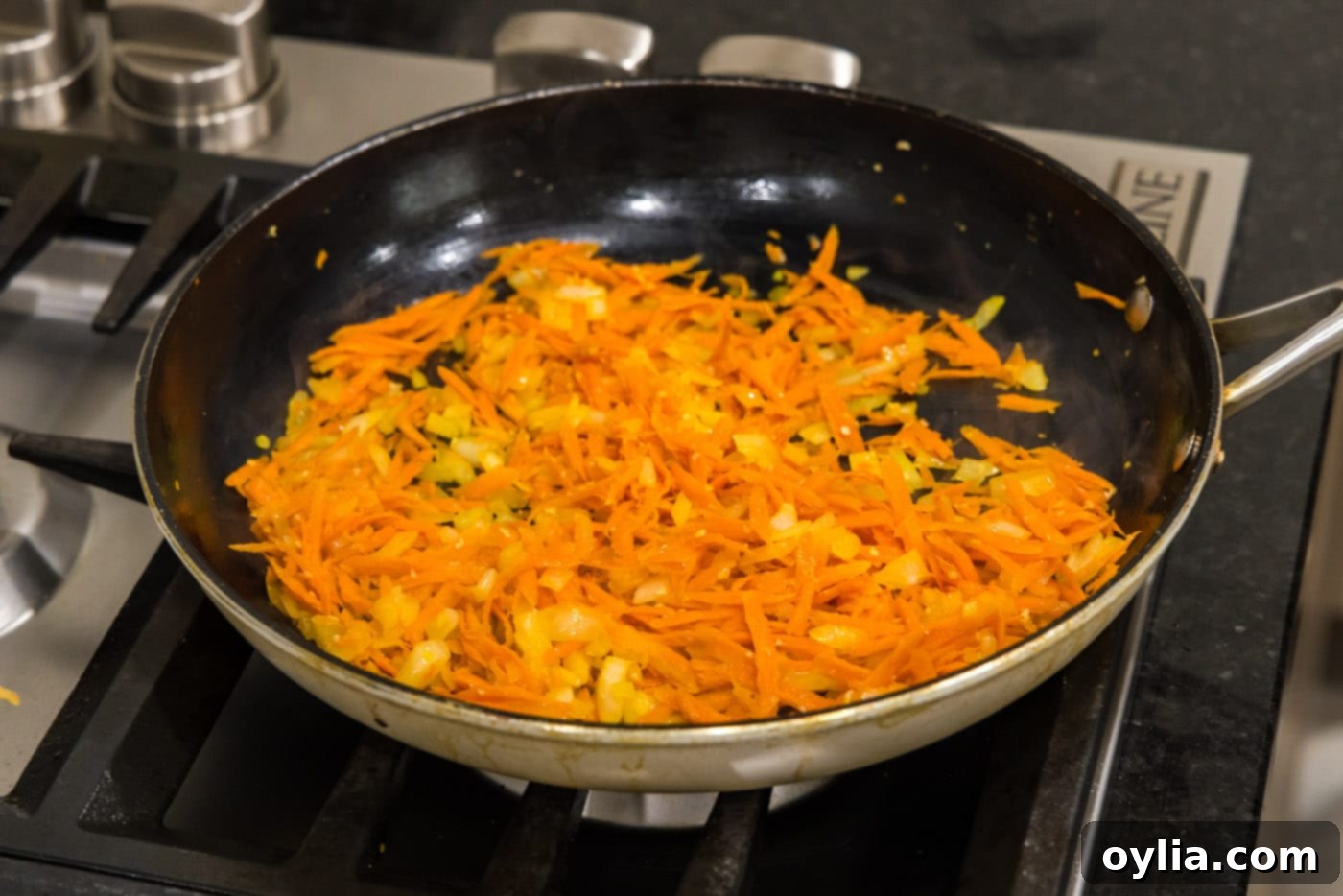 Garlic, onion, and shredded carrots cooking in a skillet, becoming softened and fragrant.