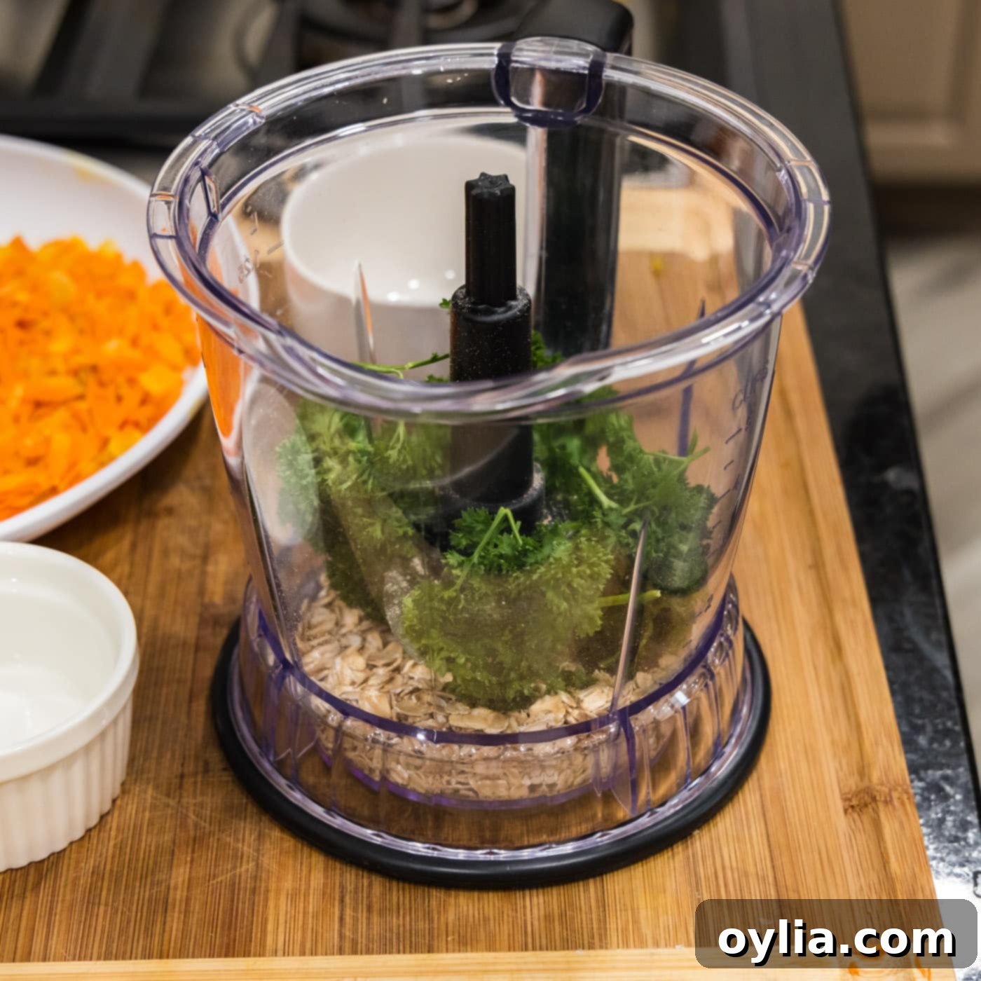 Oats and fresh parsley are in the bowl of a food processor, ready to be pulsed.