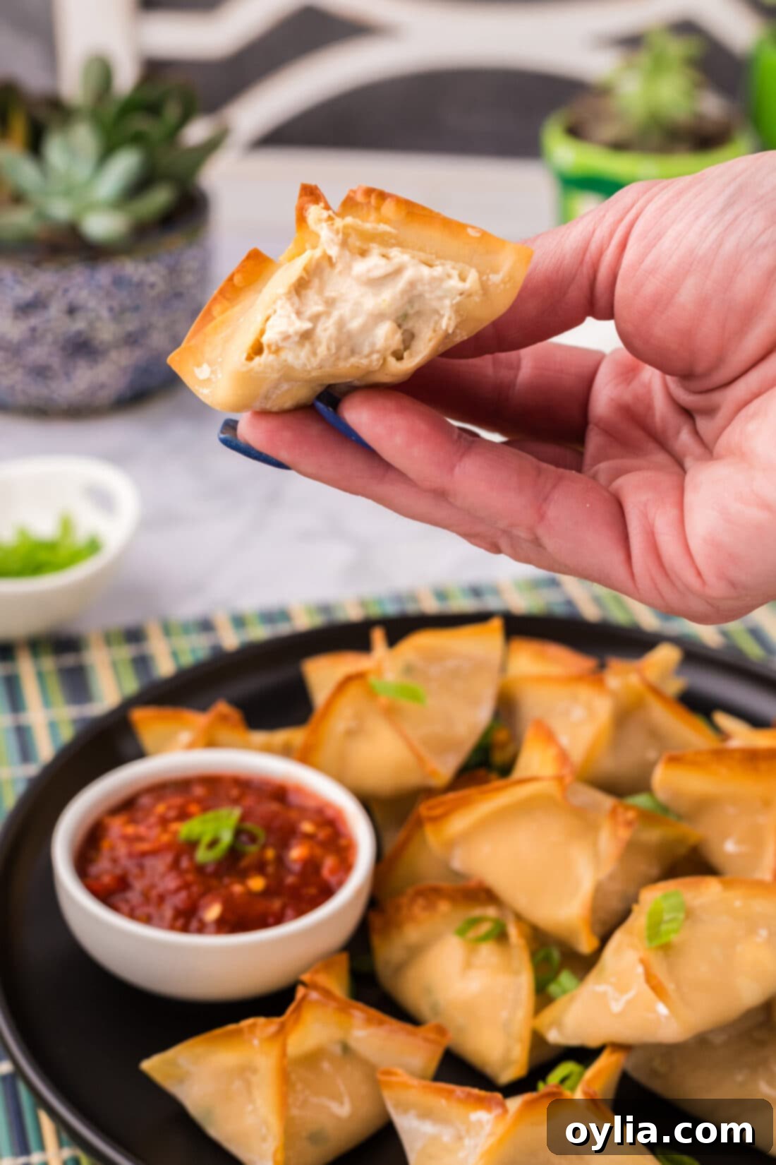 Hand holding up half of a Crab Rangoon showing the inside filling