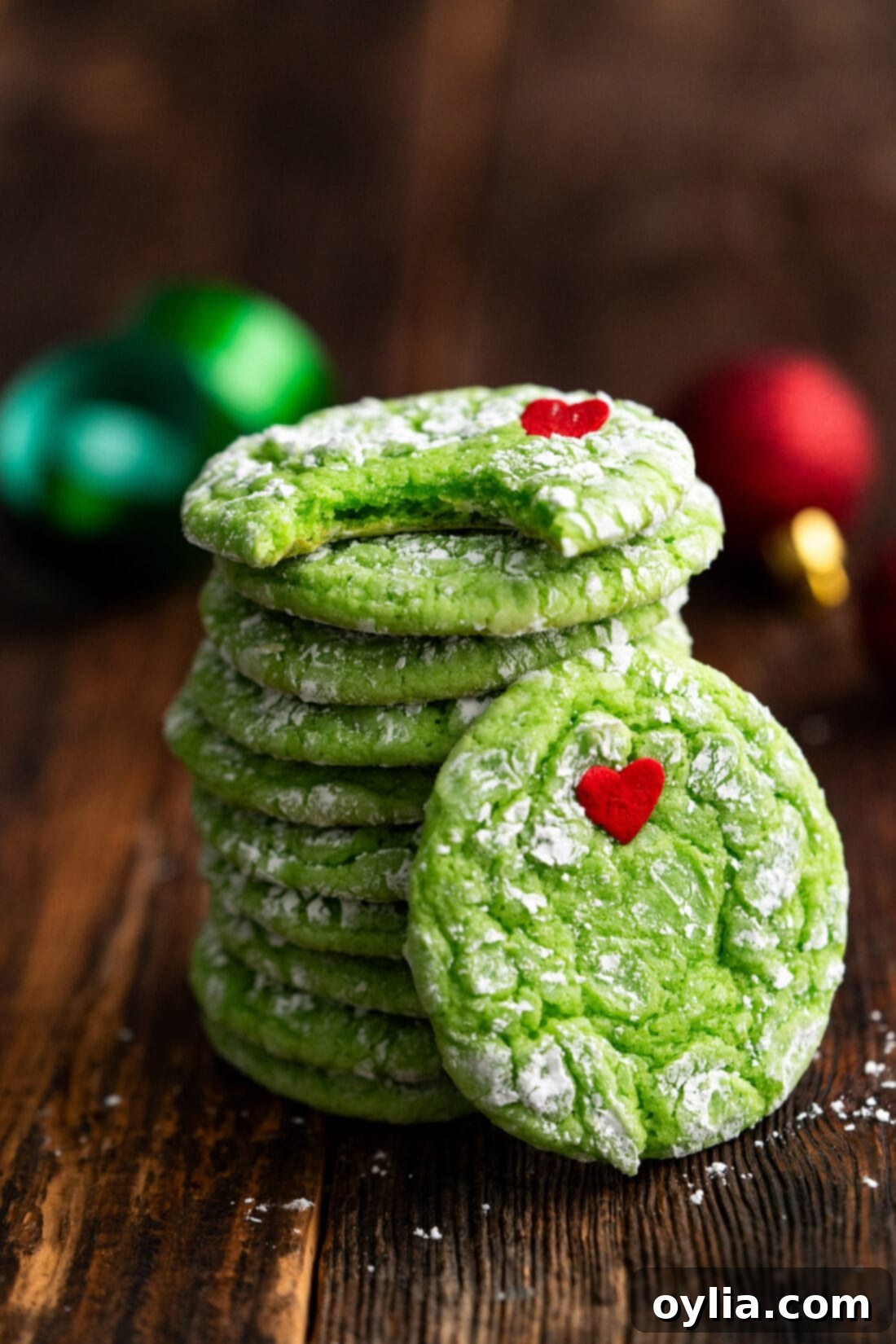 Grinchy Holiday Cookies 2 Stack of Grinch Cookies with a bite taken out of the top cookie, showing their vibrant green color and red heart, dusted with powdered sugar.