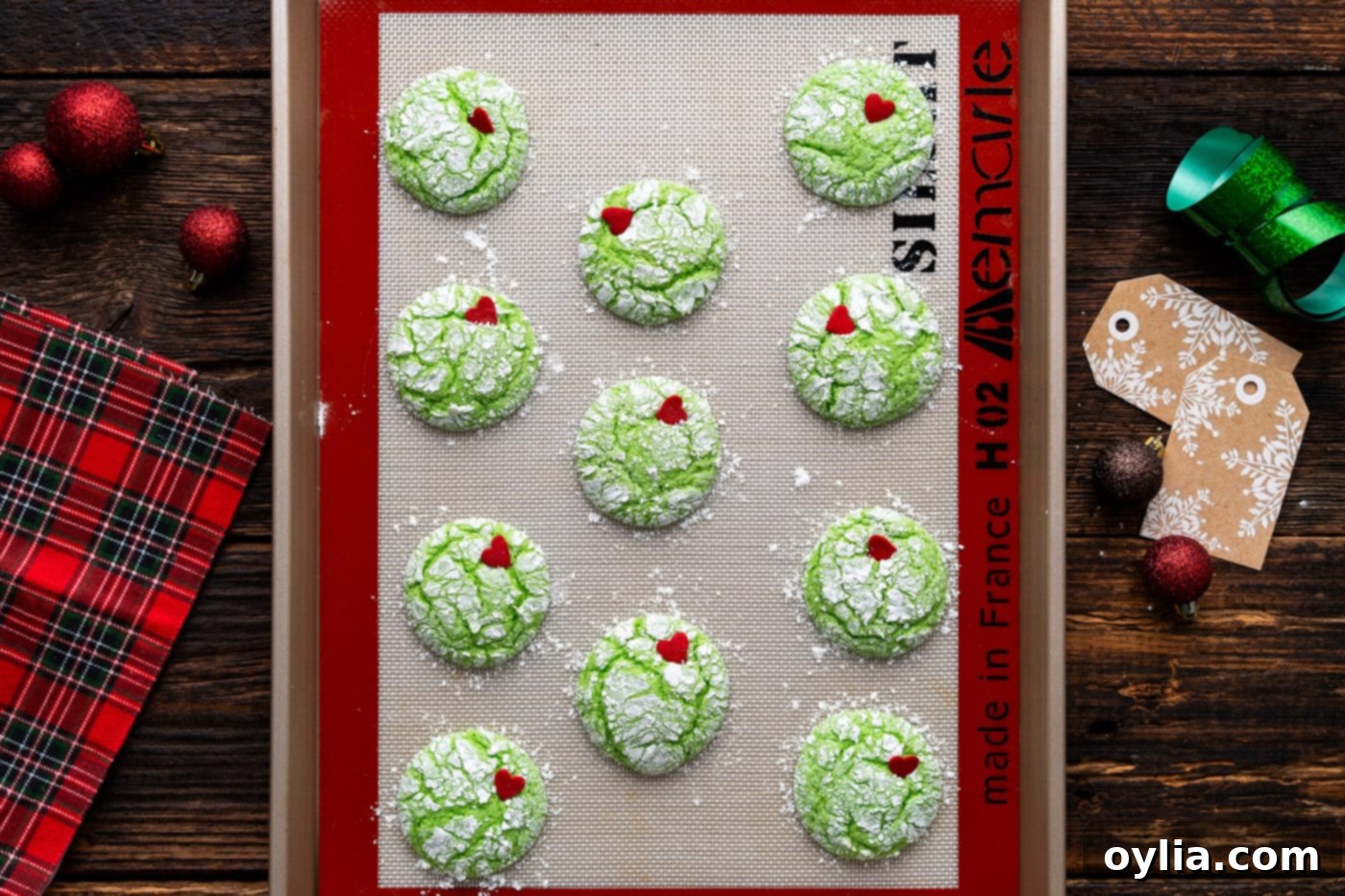 Easy Grinch cookies with vibrant red candy hearts freshly placed on each warm, green cookie.
