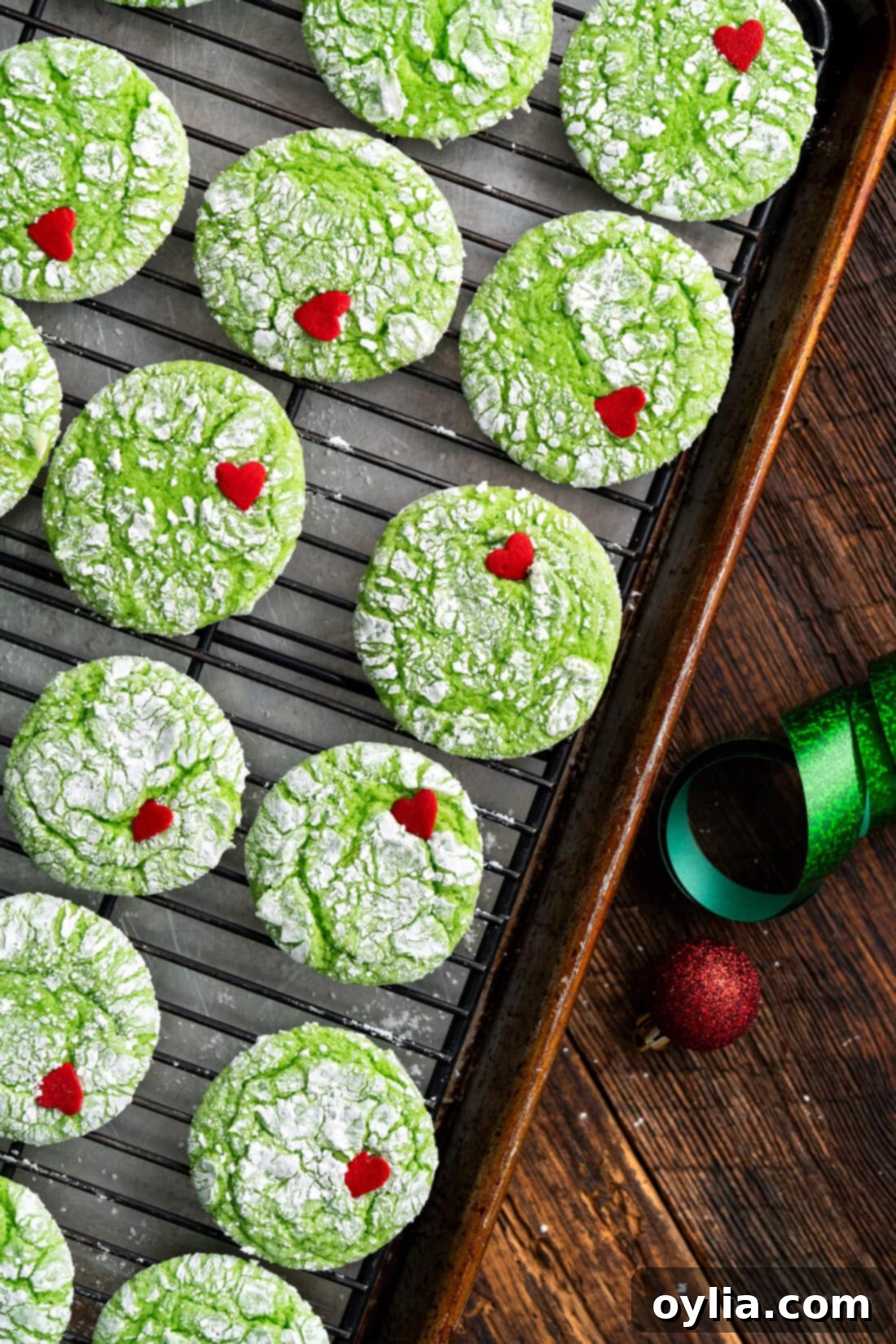Grinchy Holiday Cookies 13 Grinch Cookies cooling on a wire rack, showing off their perfect green color, white powdered sugar coating, and red candy heart.