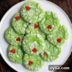 Grinchy Holiday Cookies 14 Overhead photo of a plate of Grinch Cookies, perfectly round, green, with white powdered sugar and a red heart.