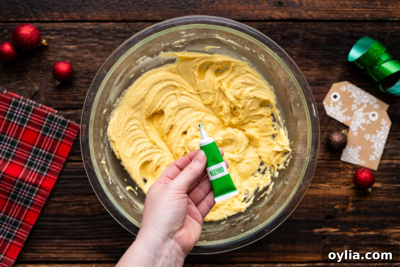 Adding green gel food coloring to the cake mix cookie dough, showing the process of tinting the dough.
