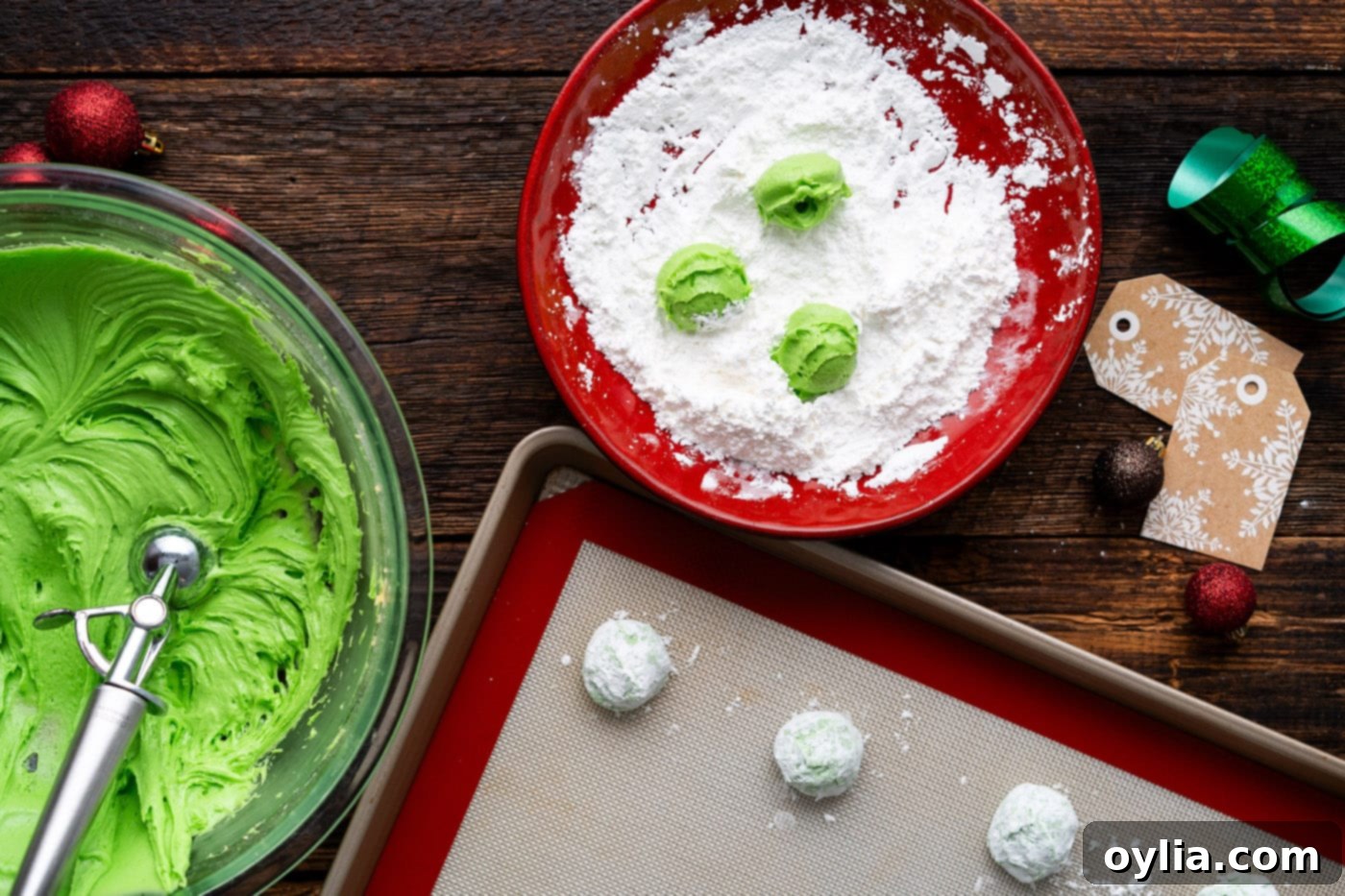 Grinch cookie dough balls rolled in powdered sugar mixture, ready to be placed on baking sheets.