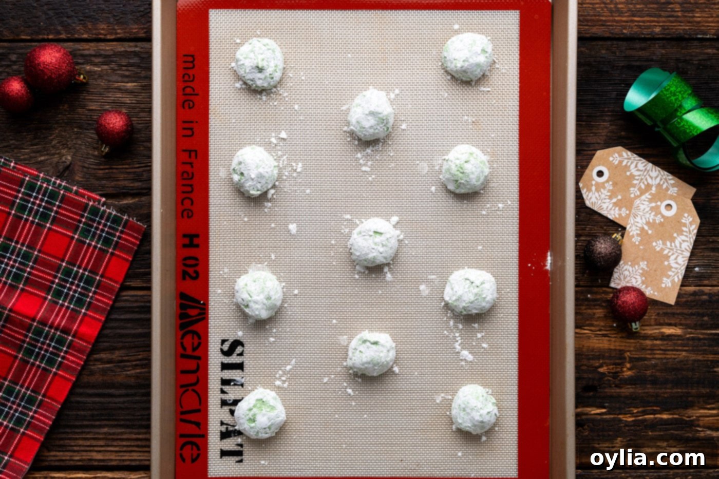 Powdered sugar coated green Grinch cookies on a baking sheet, perfectly spaced for even baking.