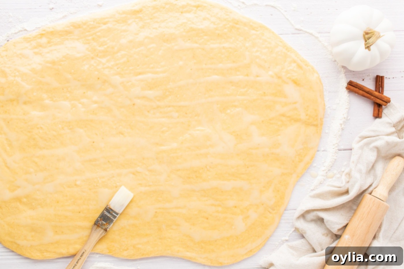 Softened butter being evenly spread across the surface of the rolled-out pumpkin cinnamon roll dough.