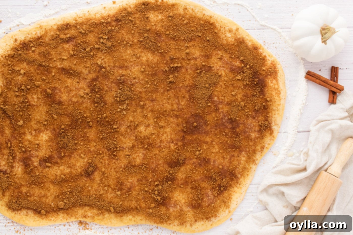 Cinnamon, nutmeg, and brown sugar mixture evenly spread over buttered cinnamon roll dough, ready to be rolled.