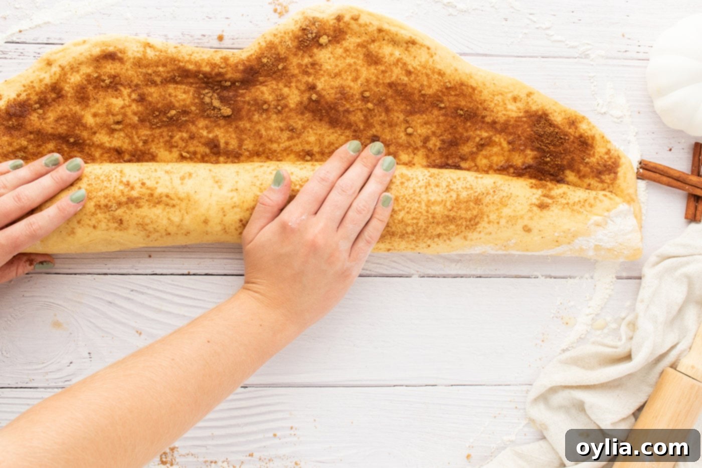 Pumpkin cinnamon roll dough being carefully rolled into a tight log after spreading with butter and spice filling.