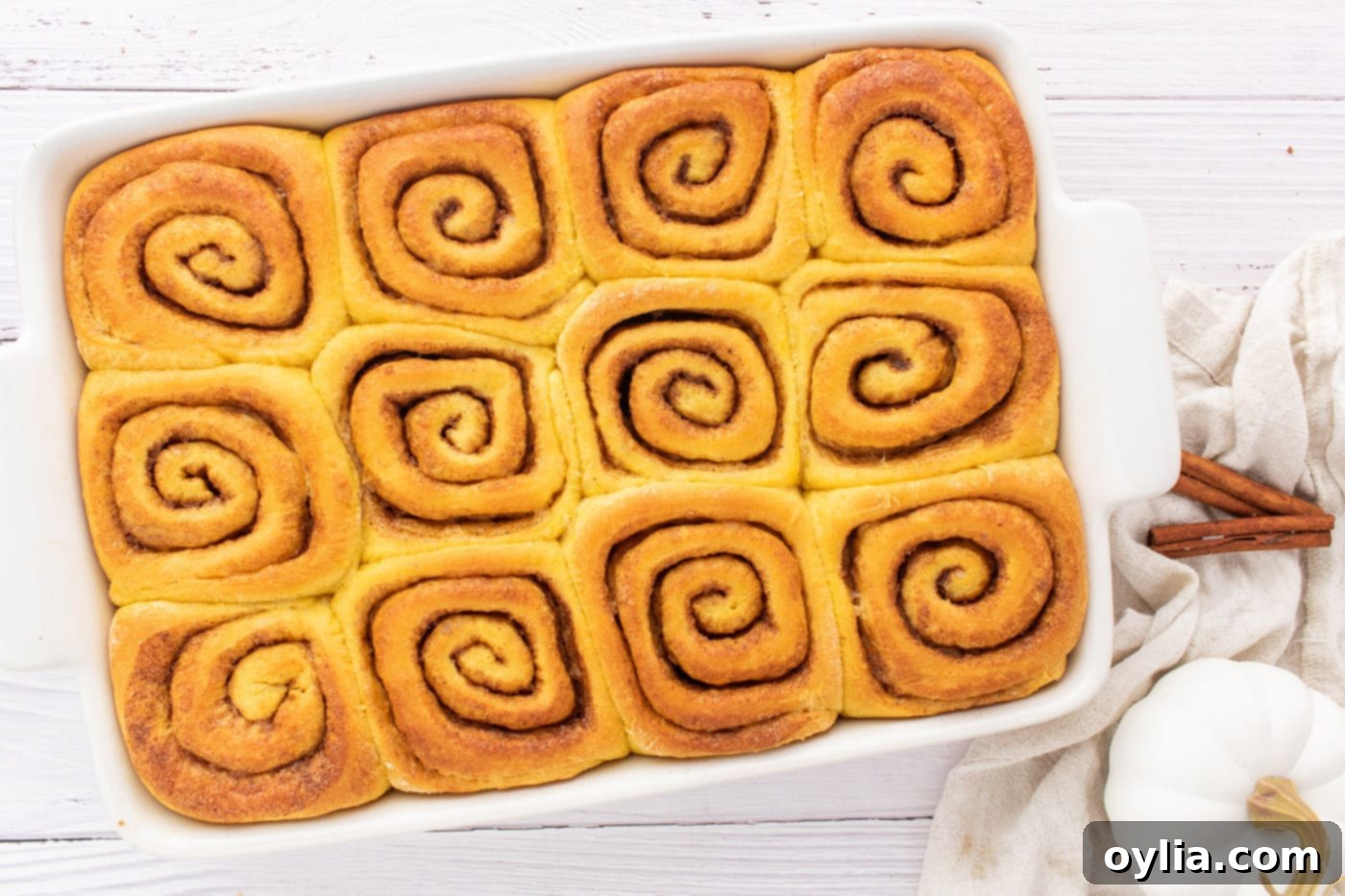 Freshly baked pumpkin cinnamon rolls, golden brown and perfectly risen, in a 9x13 inch baking pan.