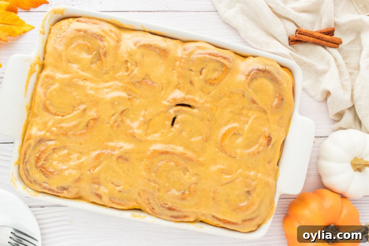 Freshly baked pumpkin cinnamon rolls generously topped with smooth pumpkin cream cheese frosting, ready to be served.