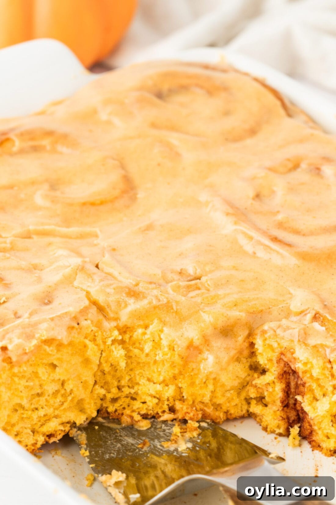 Close-up photo of a pan of freshly baked and frosted Pumpkin Cinnamon Rolls, showcasing their soft texture and gooey center.