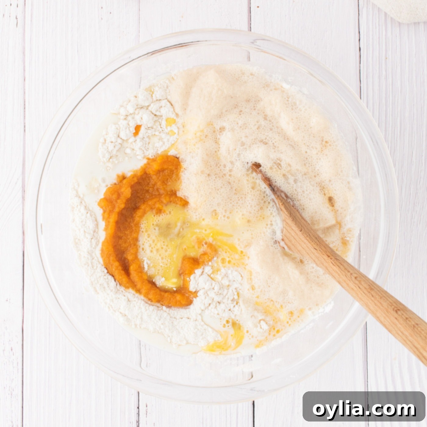 A mixing bowl with butter, eggs, vanilla extract, pumpkin puree, warm milk, and activated yeast mixture added to dry ingredients for cinnamon roll dough.