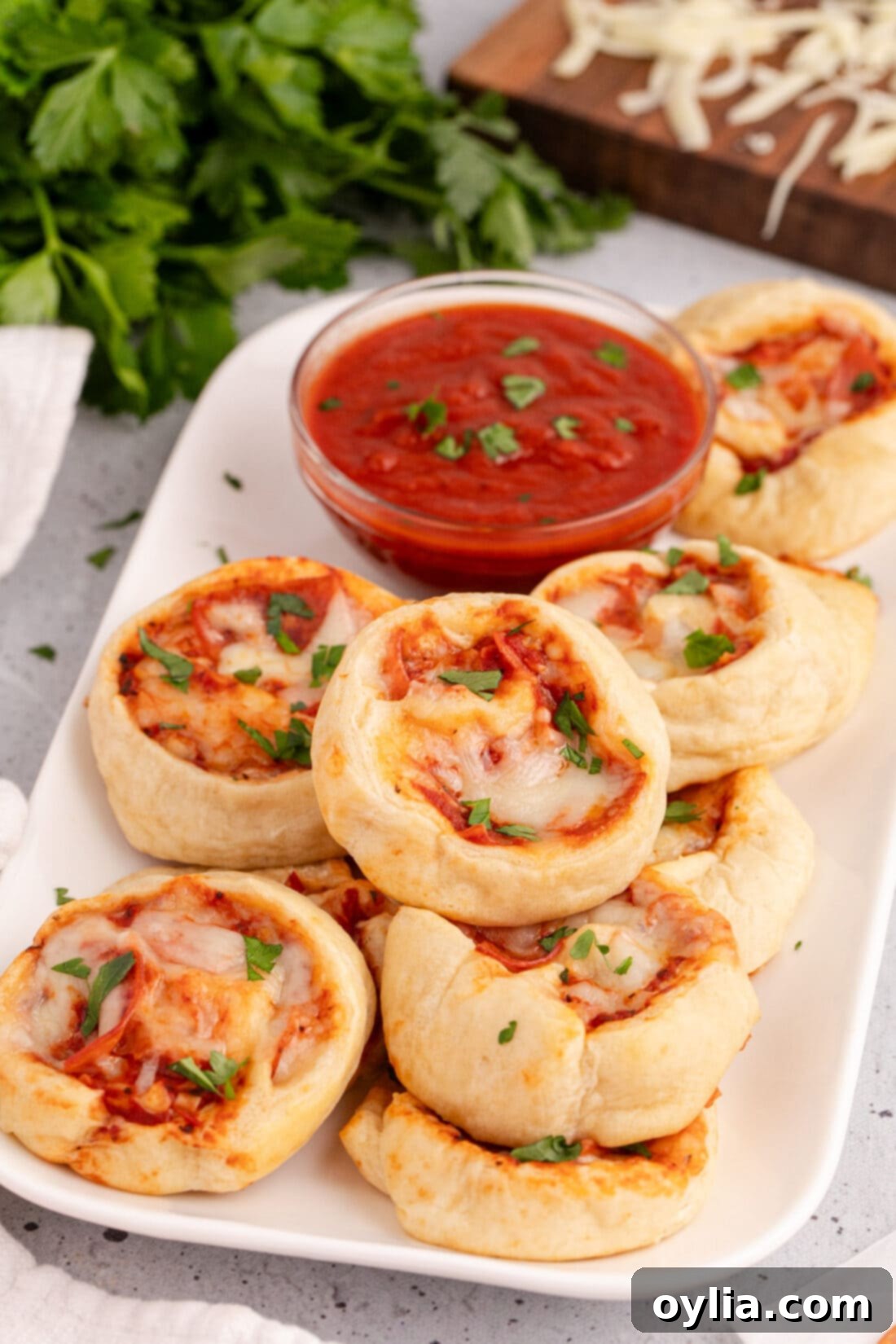 Cheesy Pizza Pinwheels 2 Delicious pizza pinwheels arranged beautifully on a platter, ready to be served with a small bowl of marinara dipping sauce.