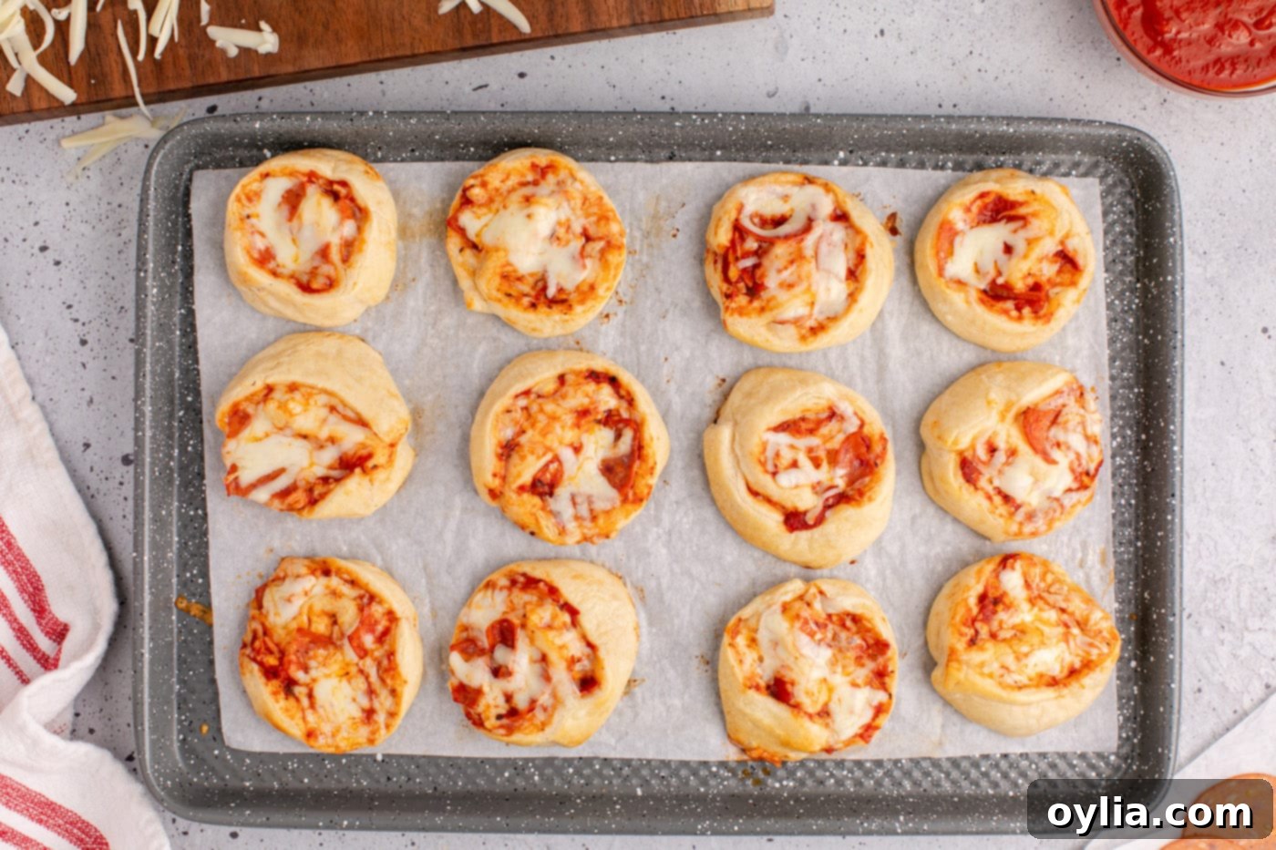 Freshly baked pepperoni pizza pinwheels, golden and bubbly, on a baking sheet.