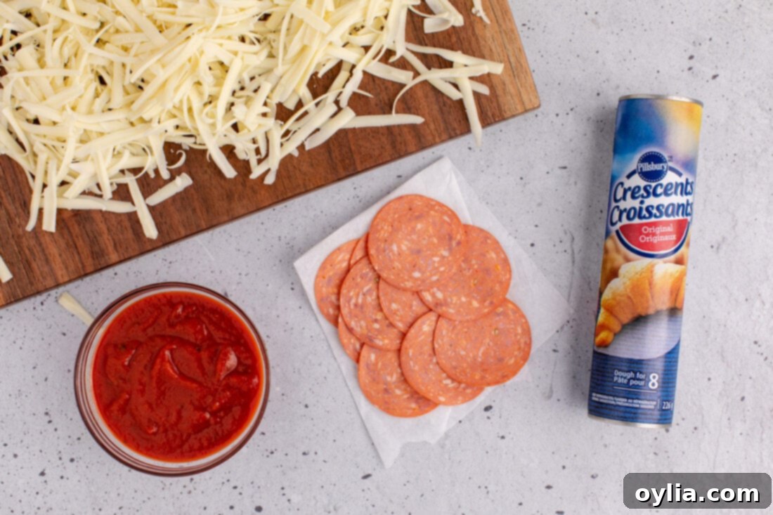 Cheesy Pizza Pinwheels 4 A flat lay photograph showcasing the simple ingredients needed for pizza pinwheels: crescent roll dough, pizza sauce, shredded mozzarella, and pepperoni slices.