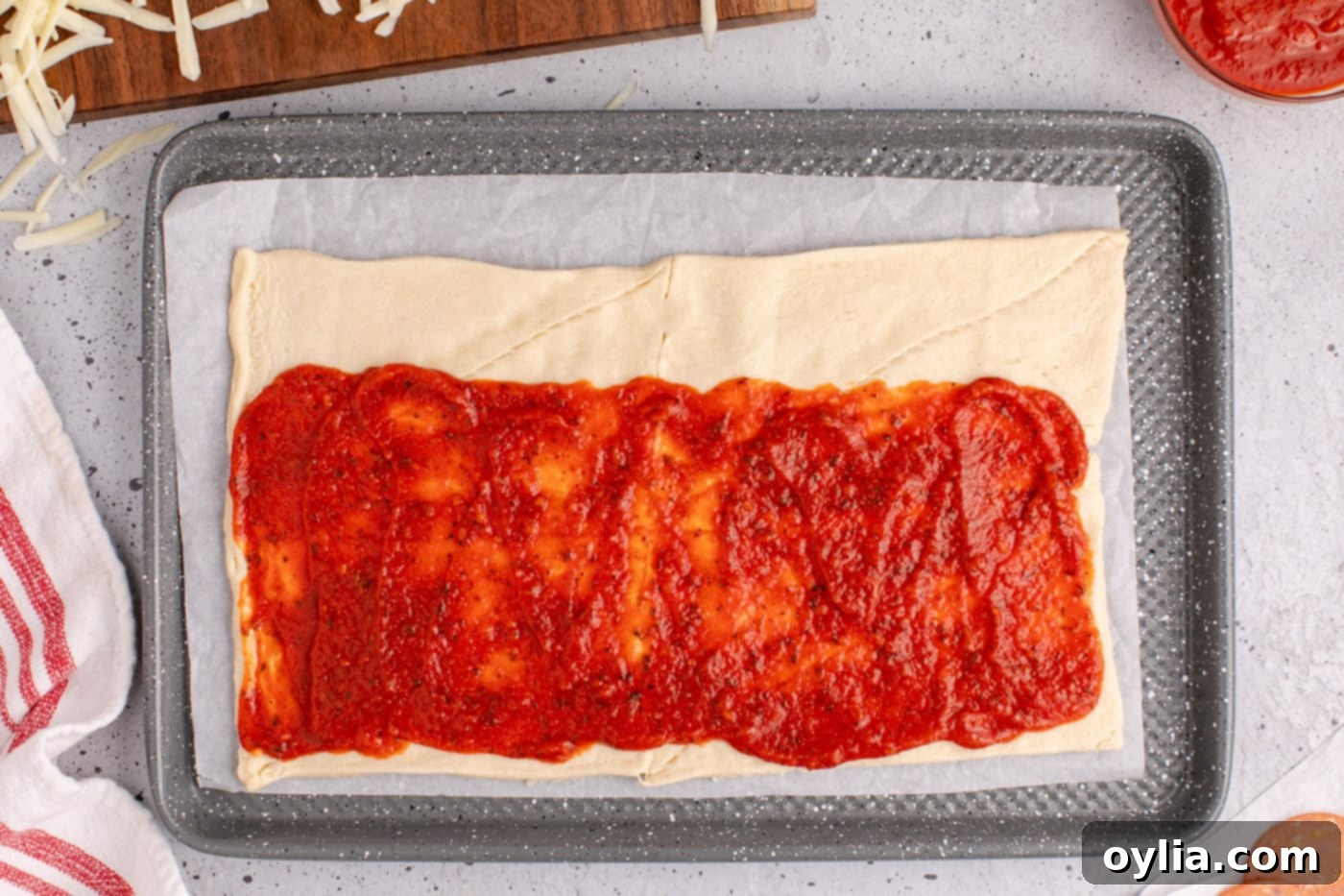 Pizza sauce evenly spread over the crescent roll dough, with a clear margin along one long edge.