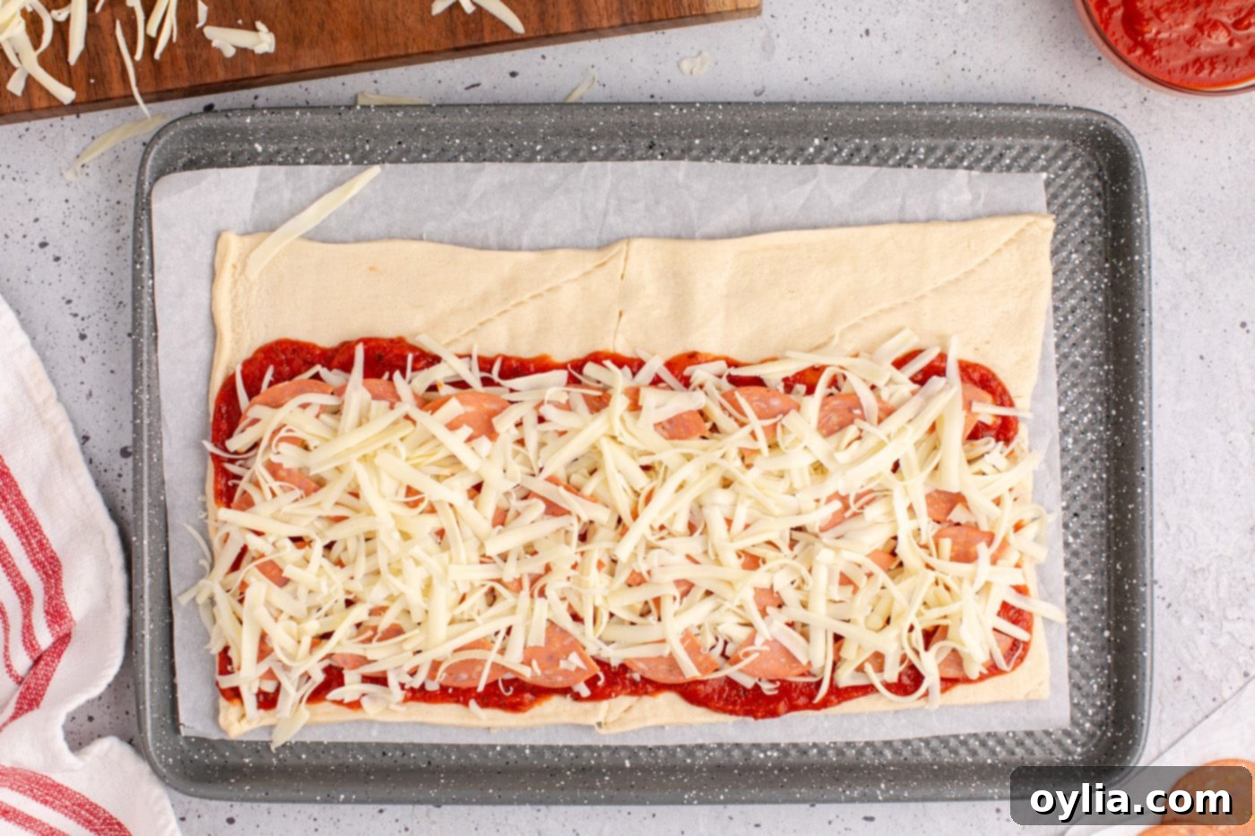 Final layer of mozzarella cheese on top of pepperoni and sauce-covered crescent roll dough.