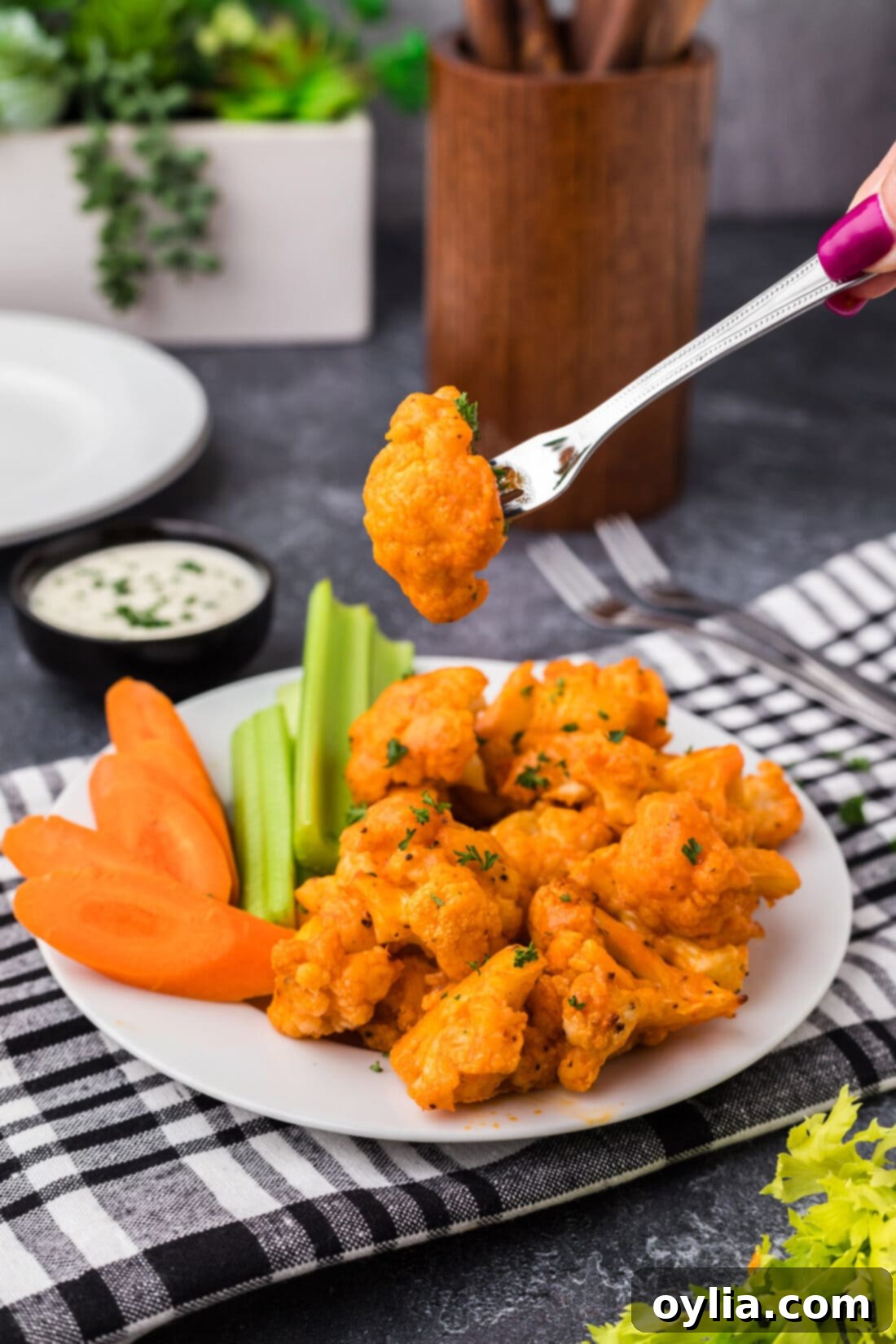 Buffalo Cauliflower on a fork held above a plate of Buffalo Cauliflower