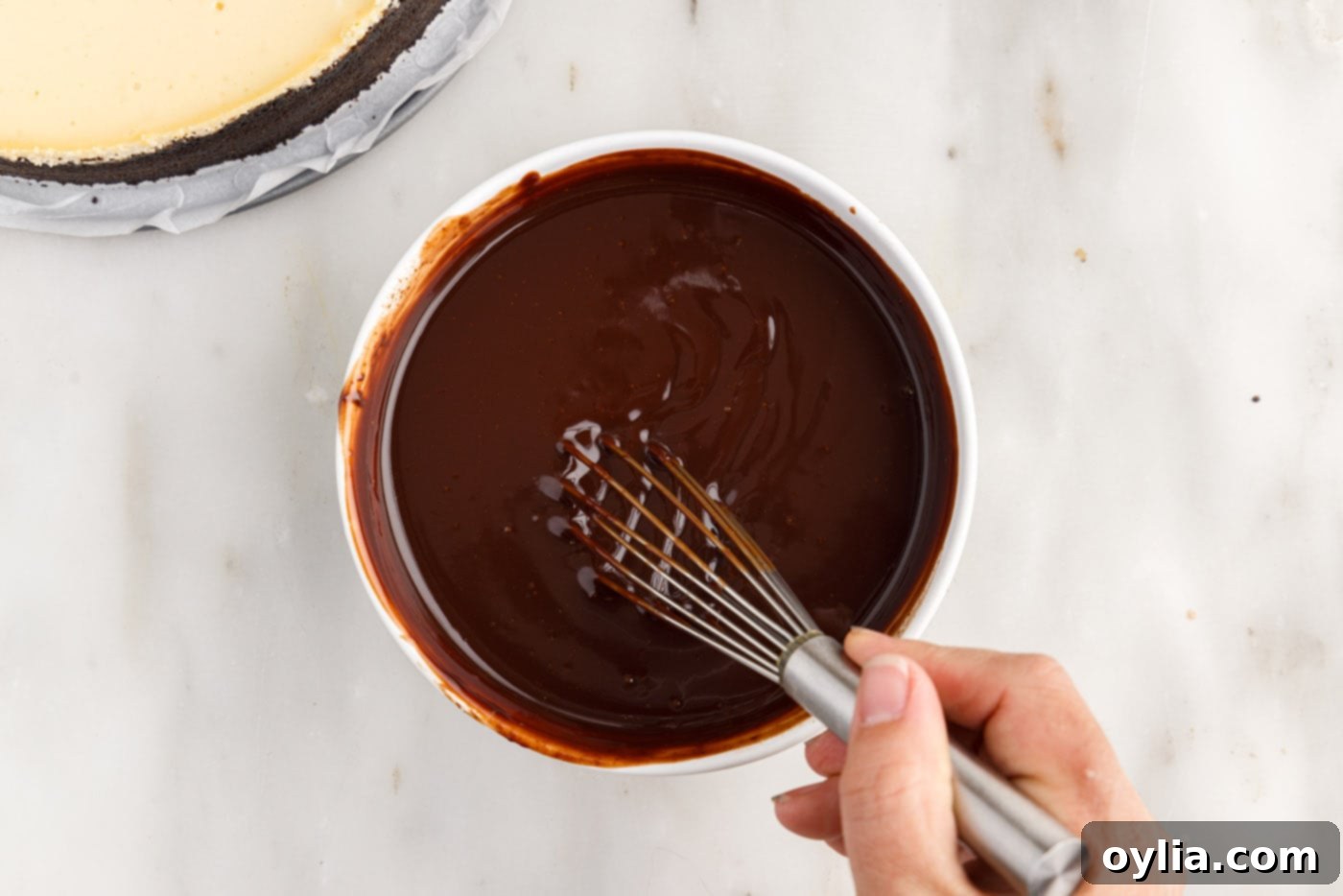Whisking melted chocolate and heavy cream together to form a smooth, glossy ganache for the Baileys Cheesecake topping.