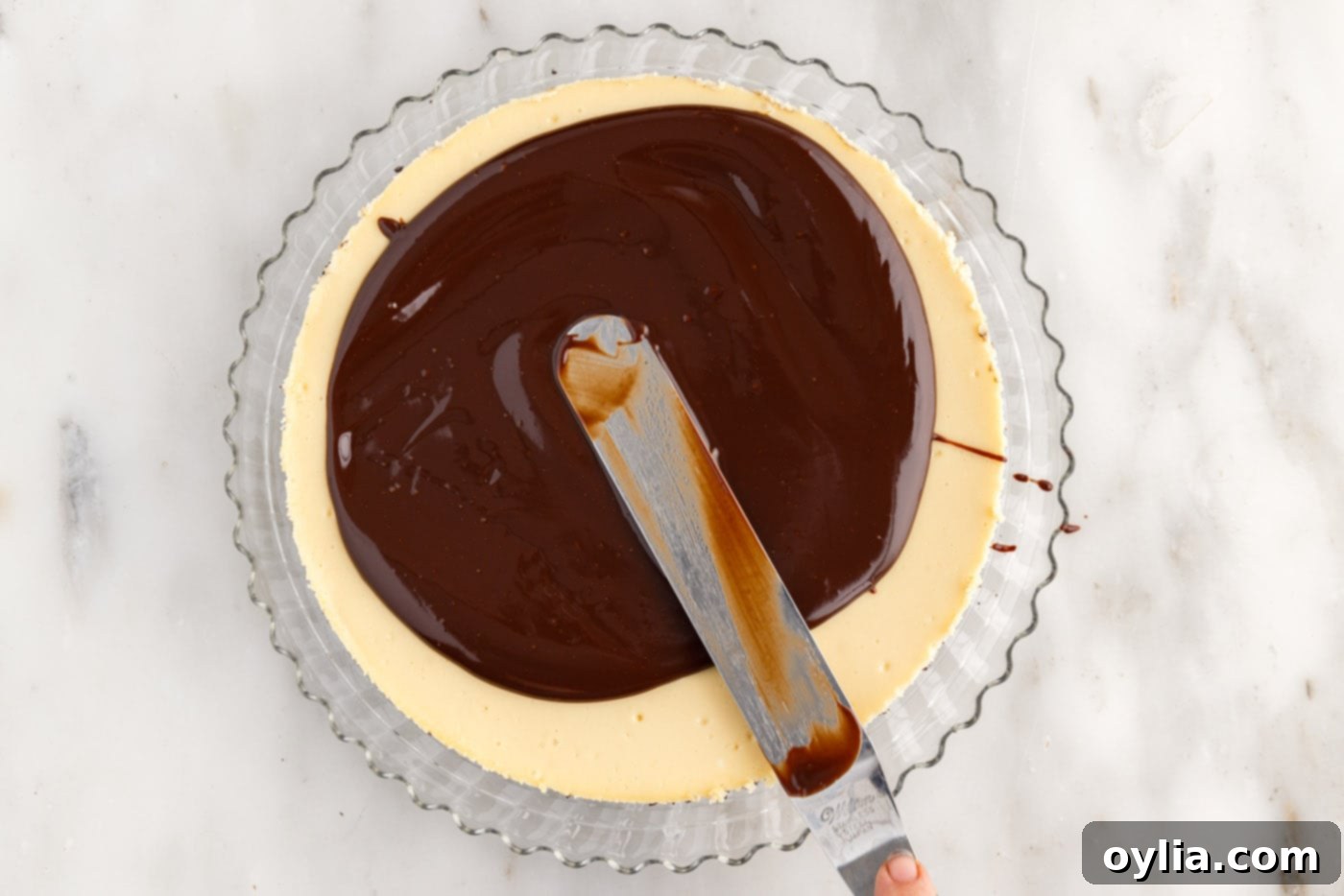 Spreading luxurious chocolate ganache over the perfectly chilled Baileys Cheesecake, letting it drip artfully over the edges.