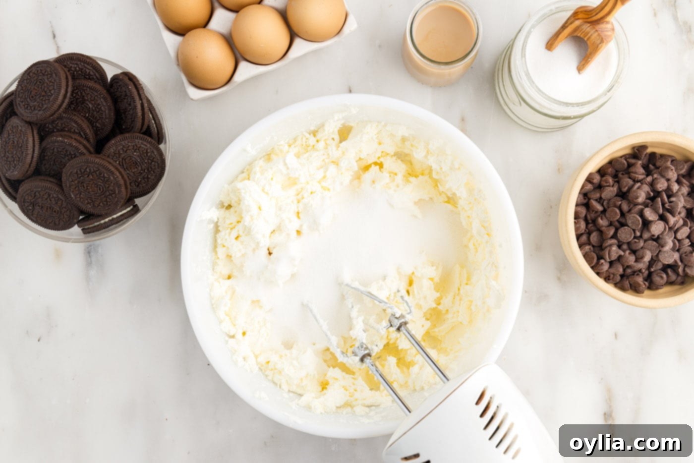 Cream cheese and granulated sugar being blended together in a mixing bowl with a hand mixer, creating a smooth base for the cheesecake filling.