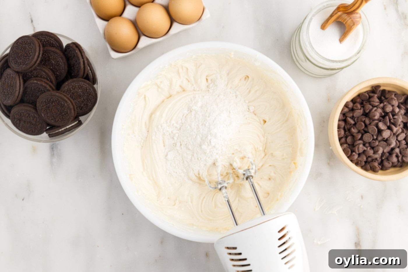 Adding all-purpose flour to the cheesecake mixture in a mixing bowl.