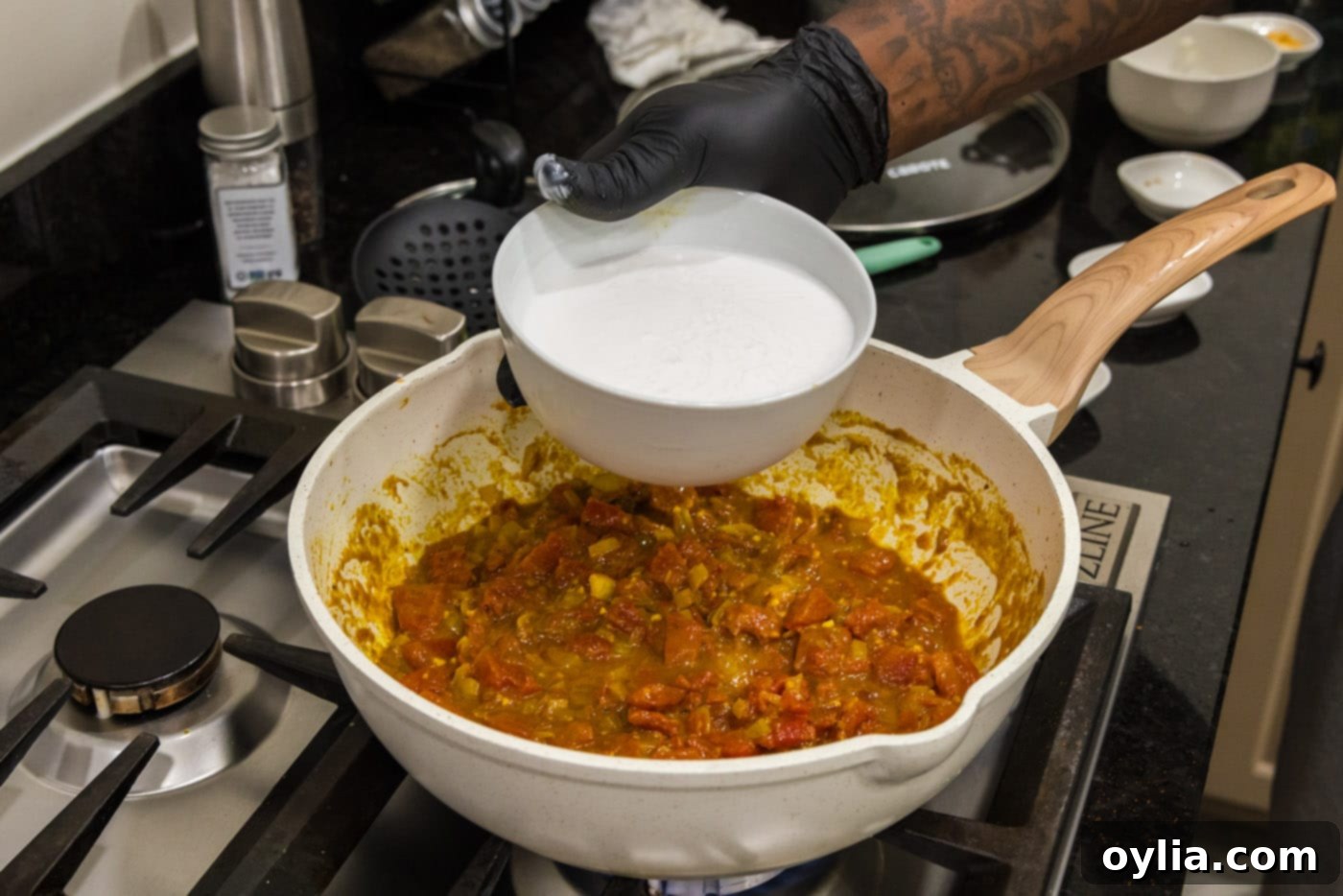pouring coconut milk into curry sauce on the stovetop