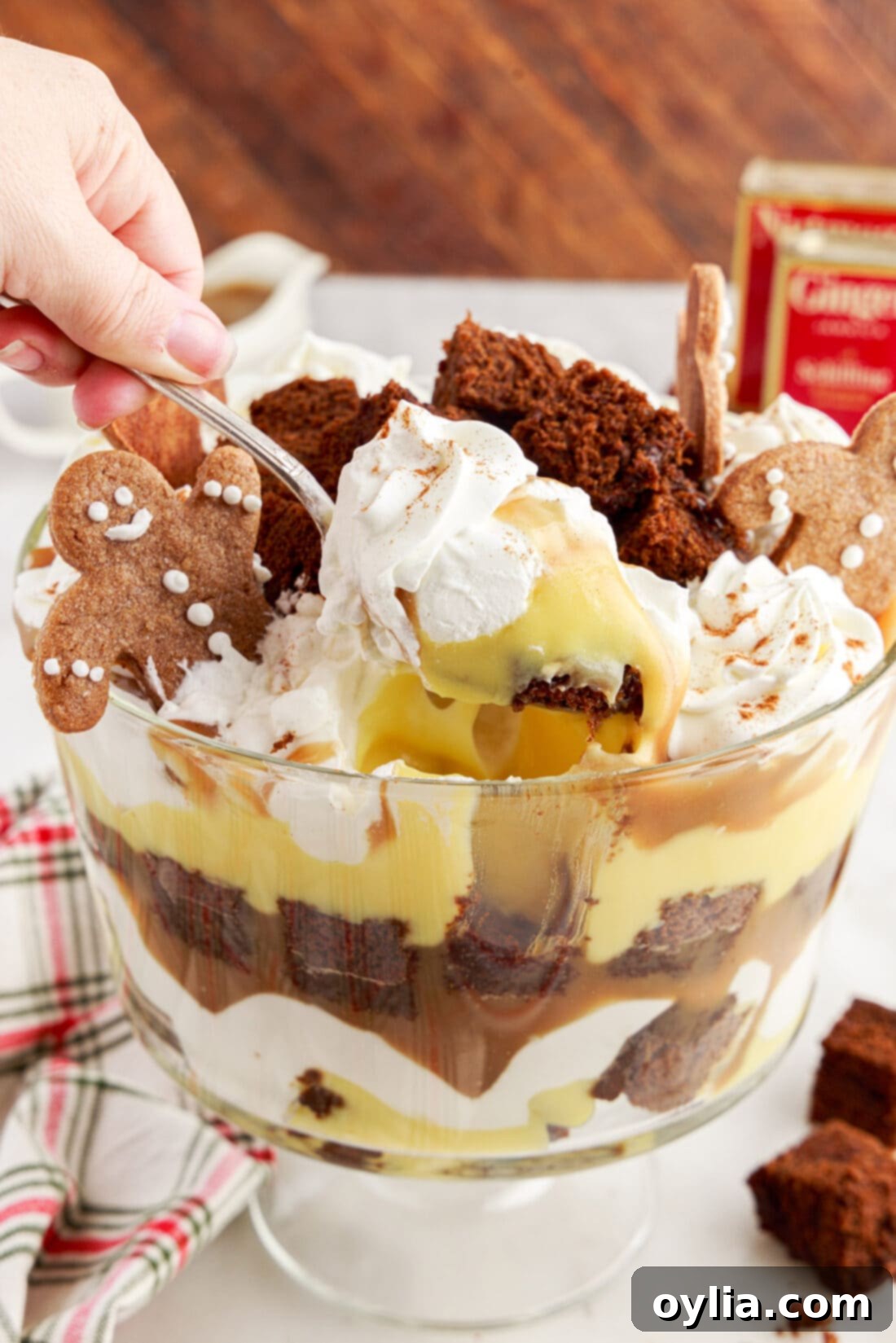 A spoonful of layered Gingerbread Trifle being scooped out of a large glass trifle bowl, showcasing its rich texture and distinct layers.