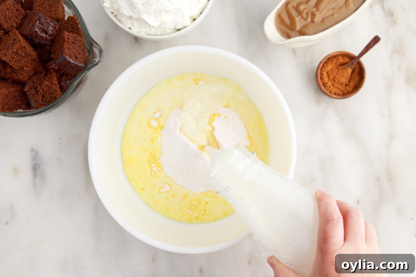 Pouring instant French vanilla pudding mix into a bowl of whole milk to prepare the creamy pudding layer for the trifle.