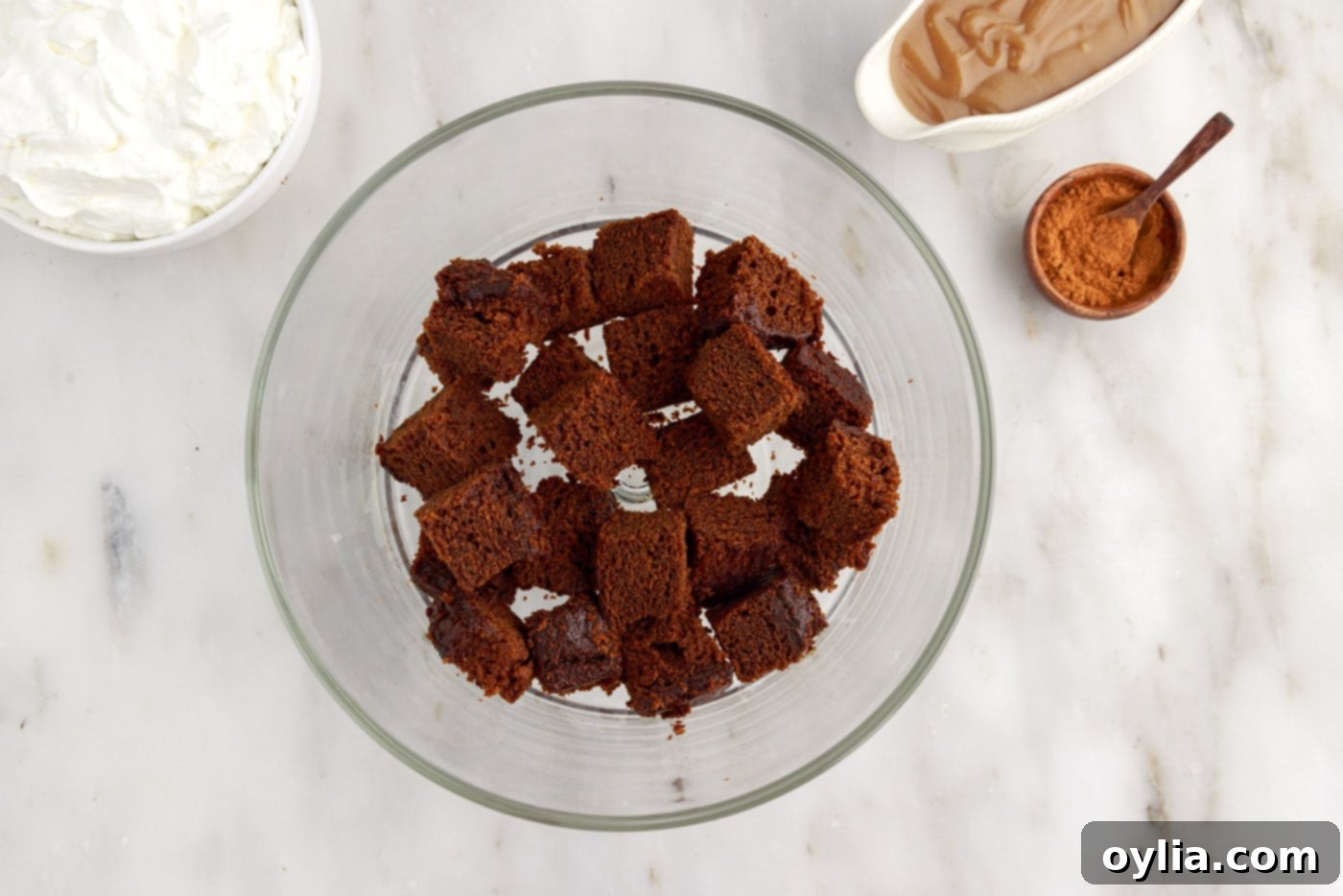 First layer of cubed gingerbread cake pieces arranged at the bottom of a clear glass trifle bowl.
