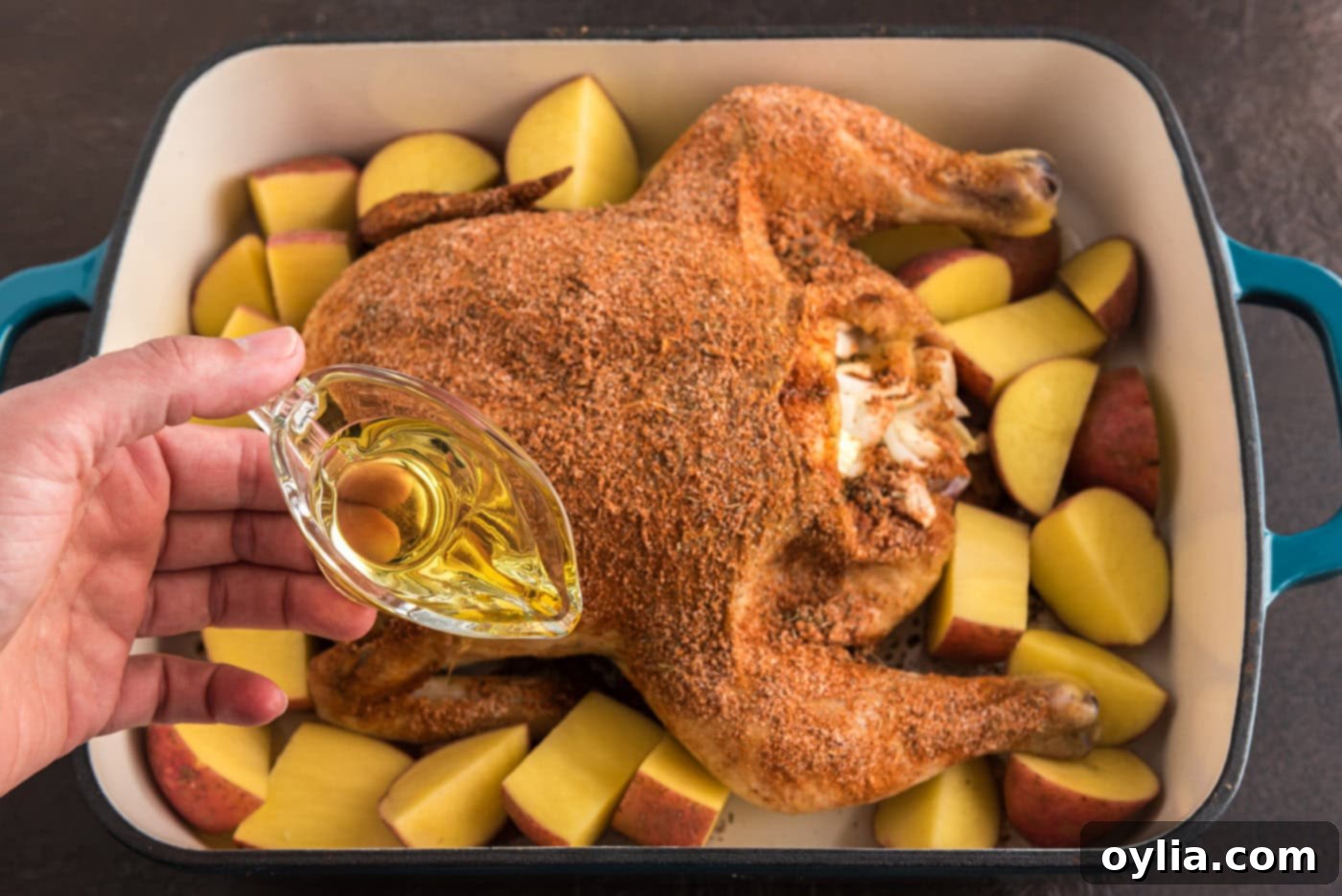 Pouring olive oil over quartered red potatoes in a pan with a whole chicken