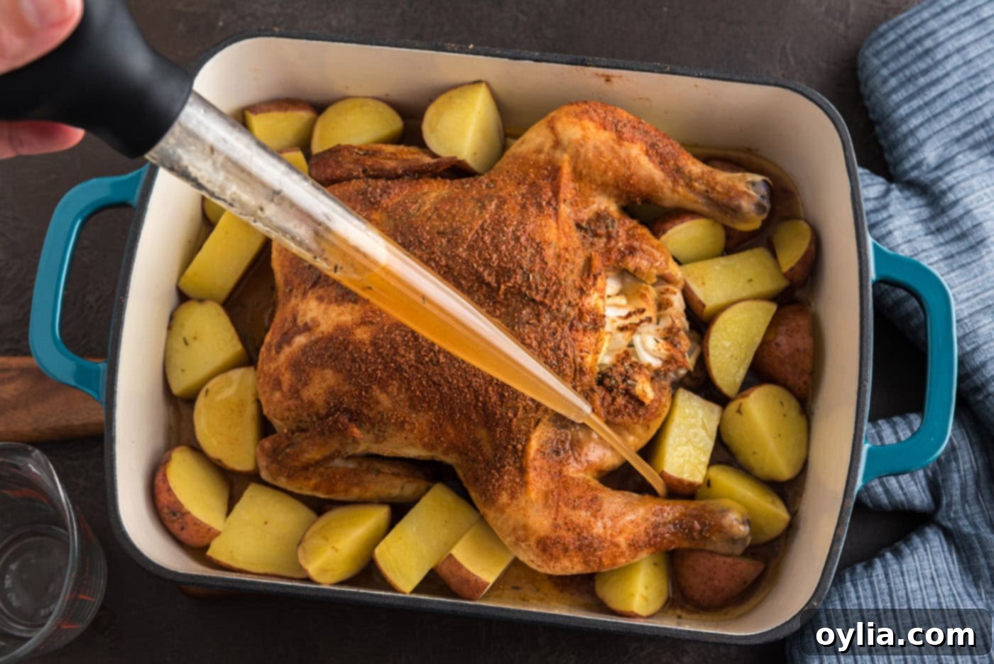 Basting chicken and potatoes in a roasting pan with pan juices