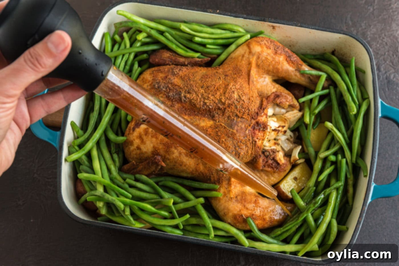 Basting chicken, potatoes, and green beans in a roasting pan