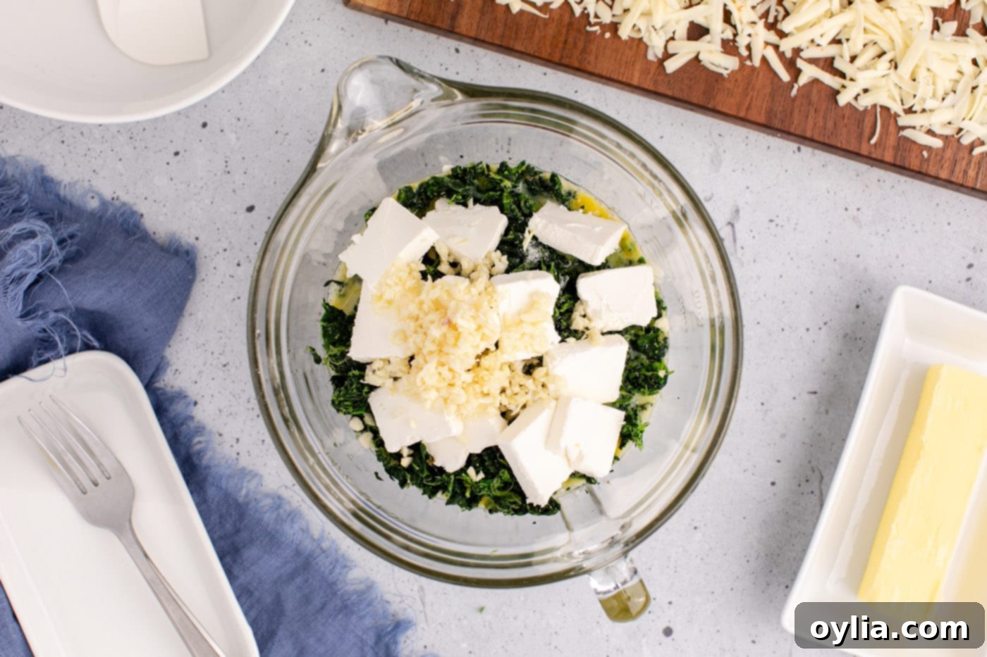 cubed cream cheese, minced garlic, and shredded pepper jack cheese are added to a bowl with whisked eggs and spinach, ready to be mixed.