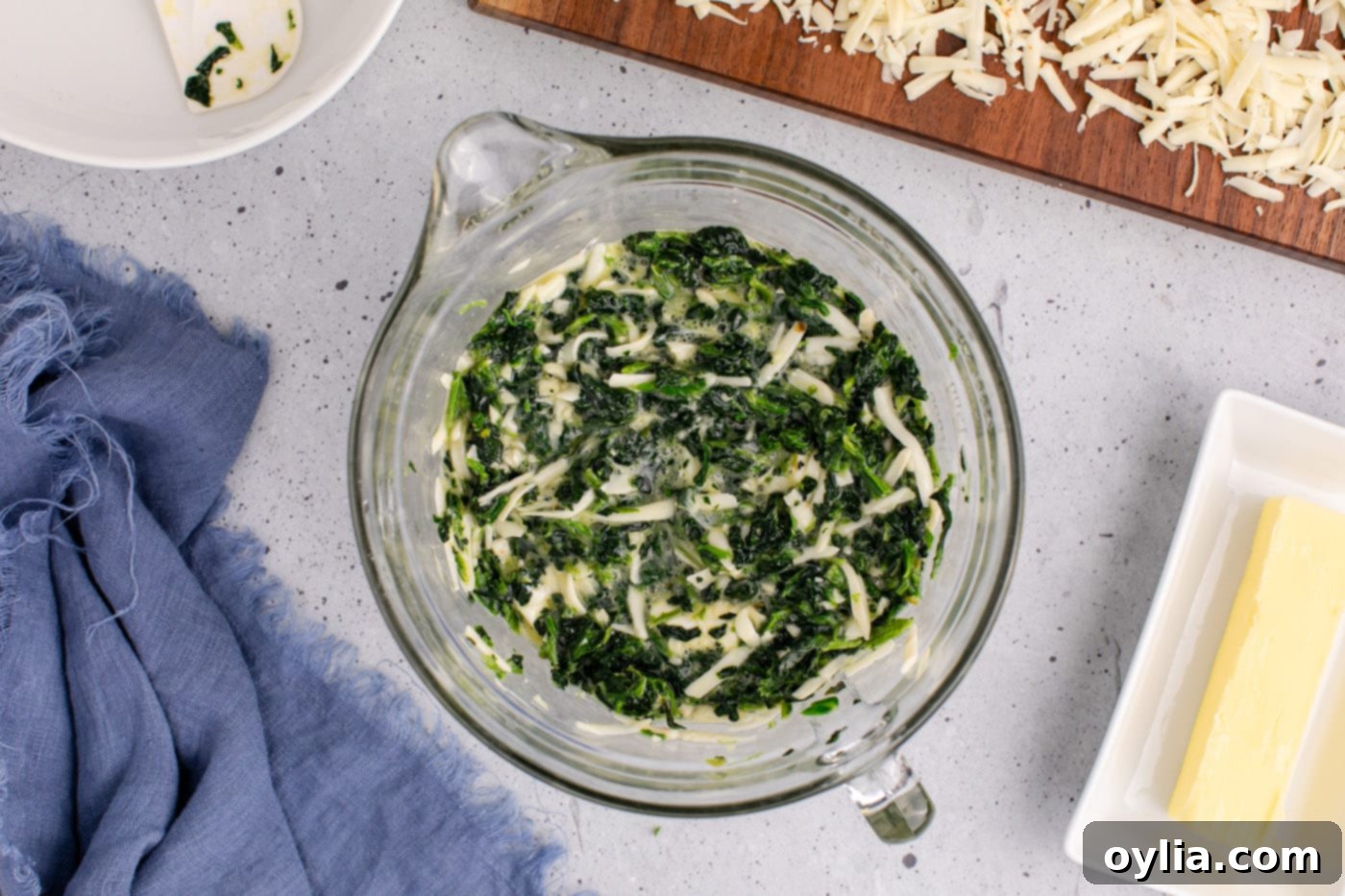 all spinach souffle ingredients mixed together in a bowl, showcasing a vibrant green and creamy mixture with visible cheese pieces, ready for the next step.