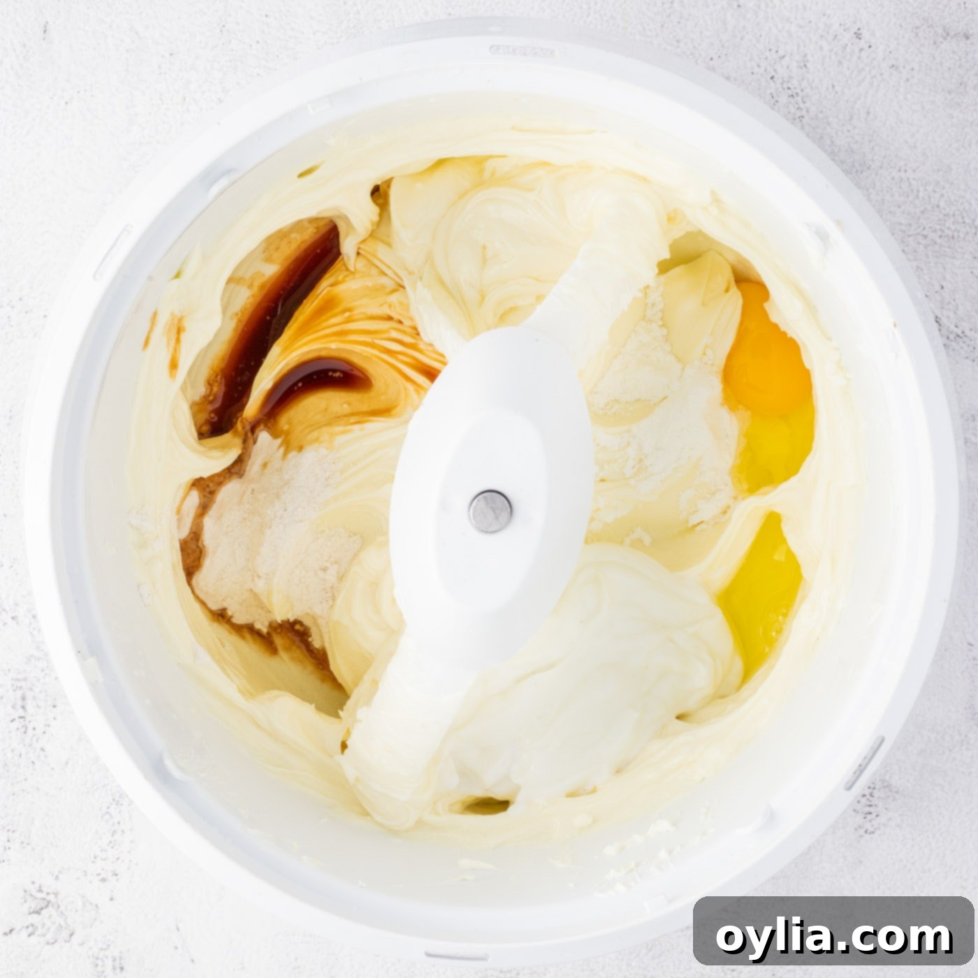 Adding eggs, vanilla, flour, and yogurt to the cheesecake mixture in a mixer.