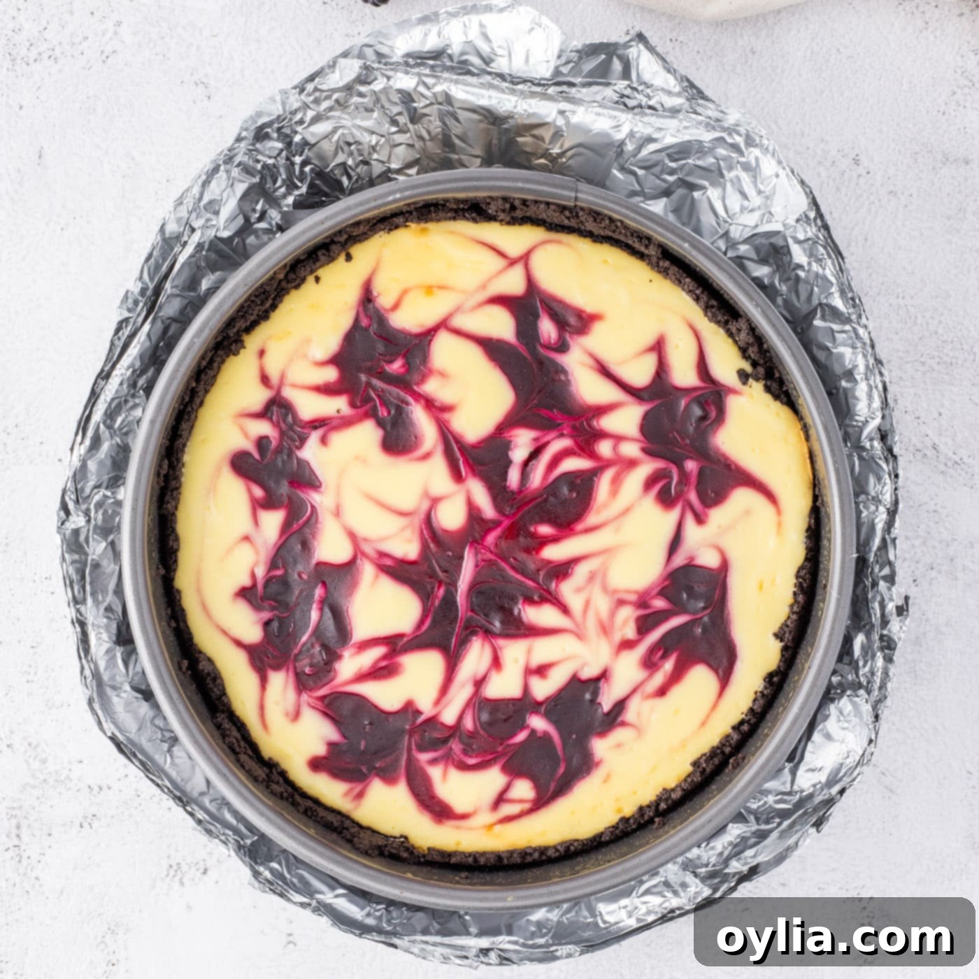 Baked blackberry swirl cheesecake still wrapped in aluminum foil, cooling in the oven.