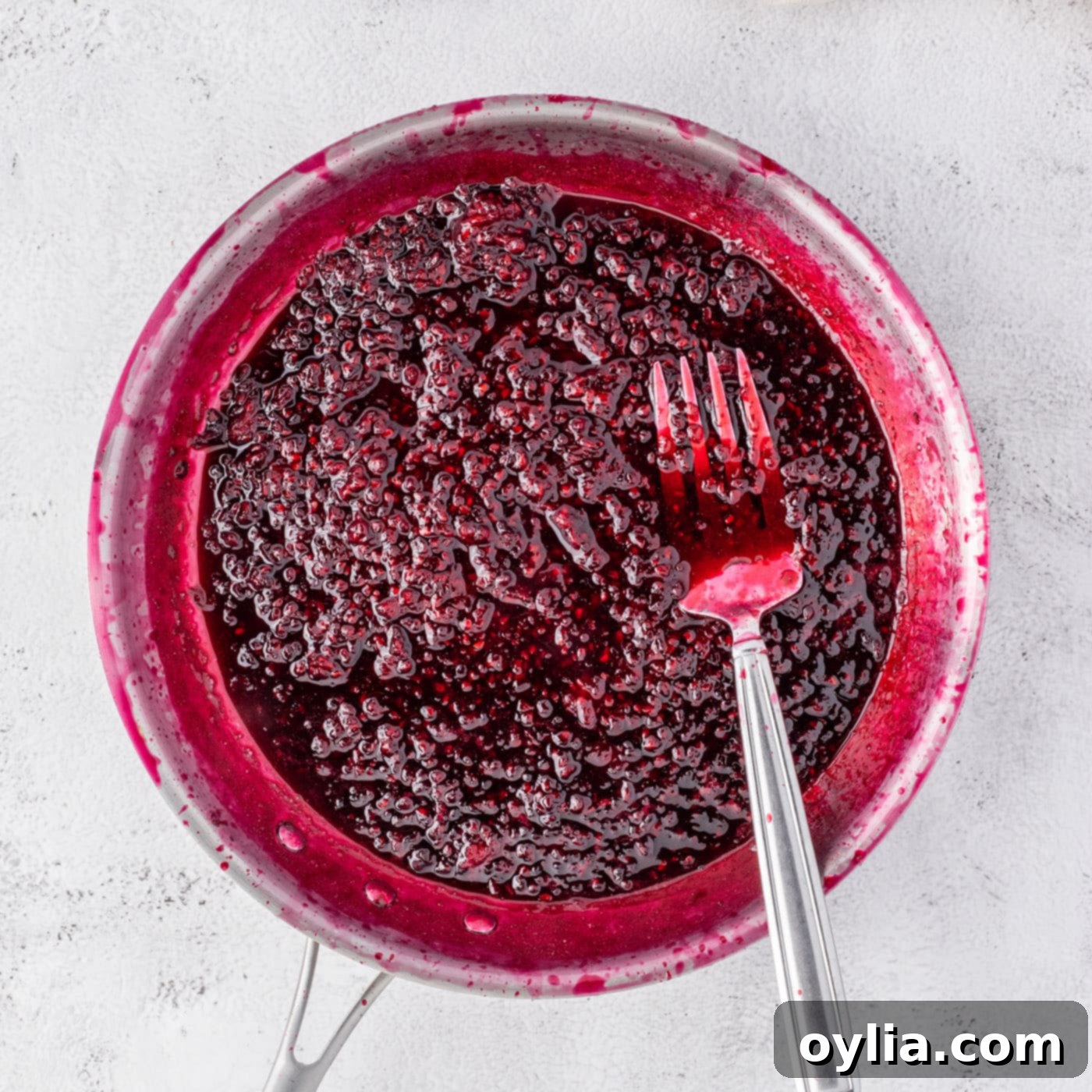 Blackberry reduction in a saucepan with a fork, showing its thickened consistency.