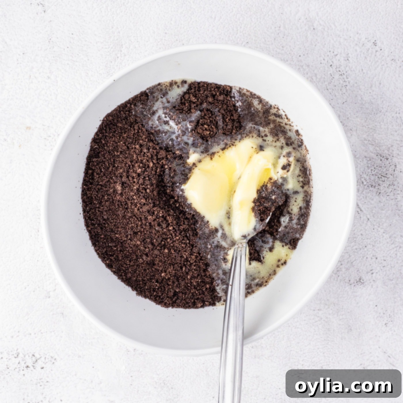 Mixing melted butter with crushed Oreo cookies for the cheesecake crust.