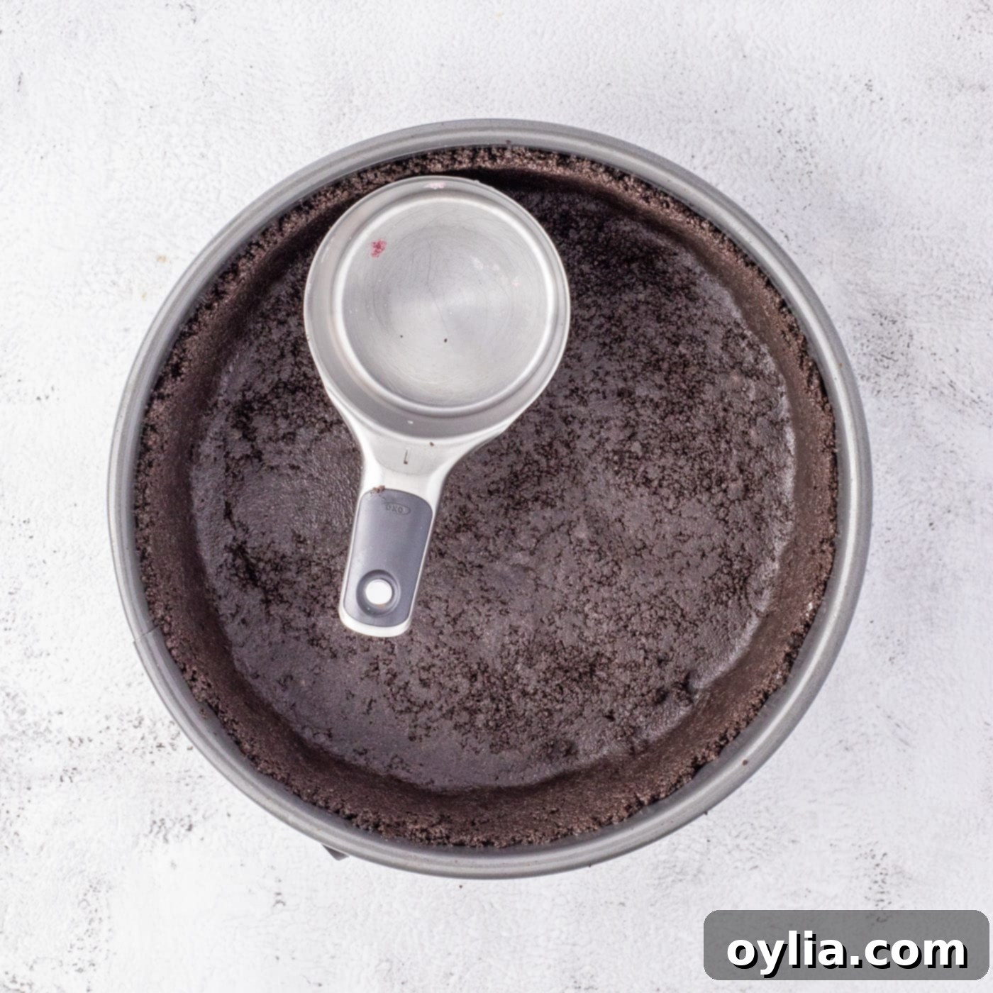 Pressing Oreo cookie crumbs into a springform pan to form the base of the cheesecake.