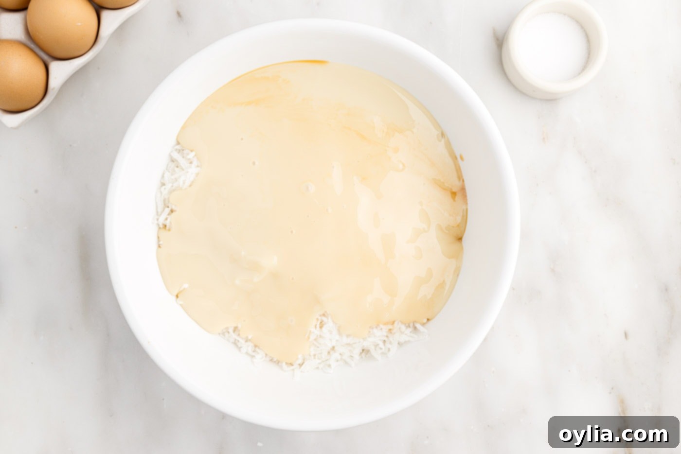 Sweetened condensed milk with shredded coconut and vanilla in a bowl before mixing