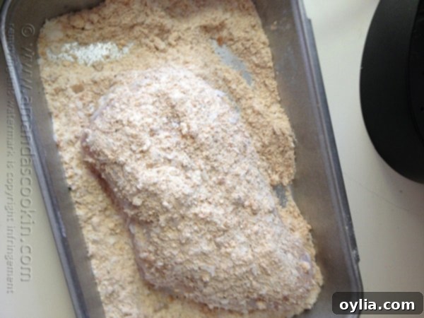 An overhead photo of a raw chicken breast in crumb coating.