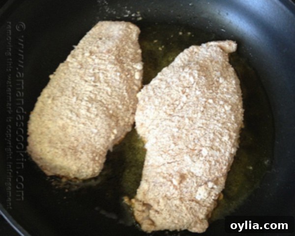 Two chicken breasts covered in crumb coating in a skillet.
