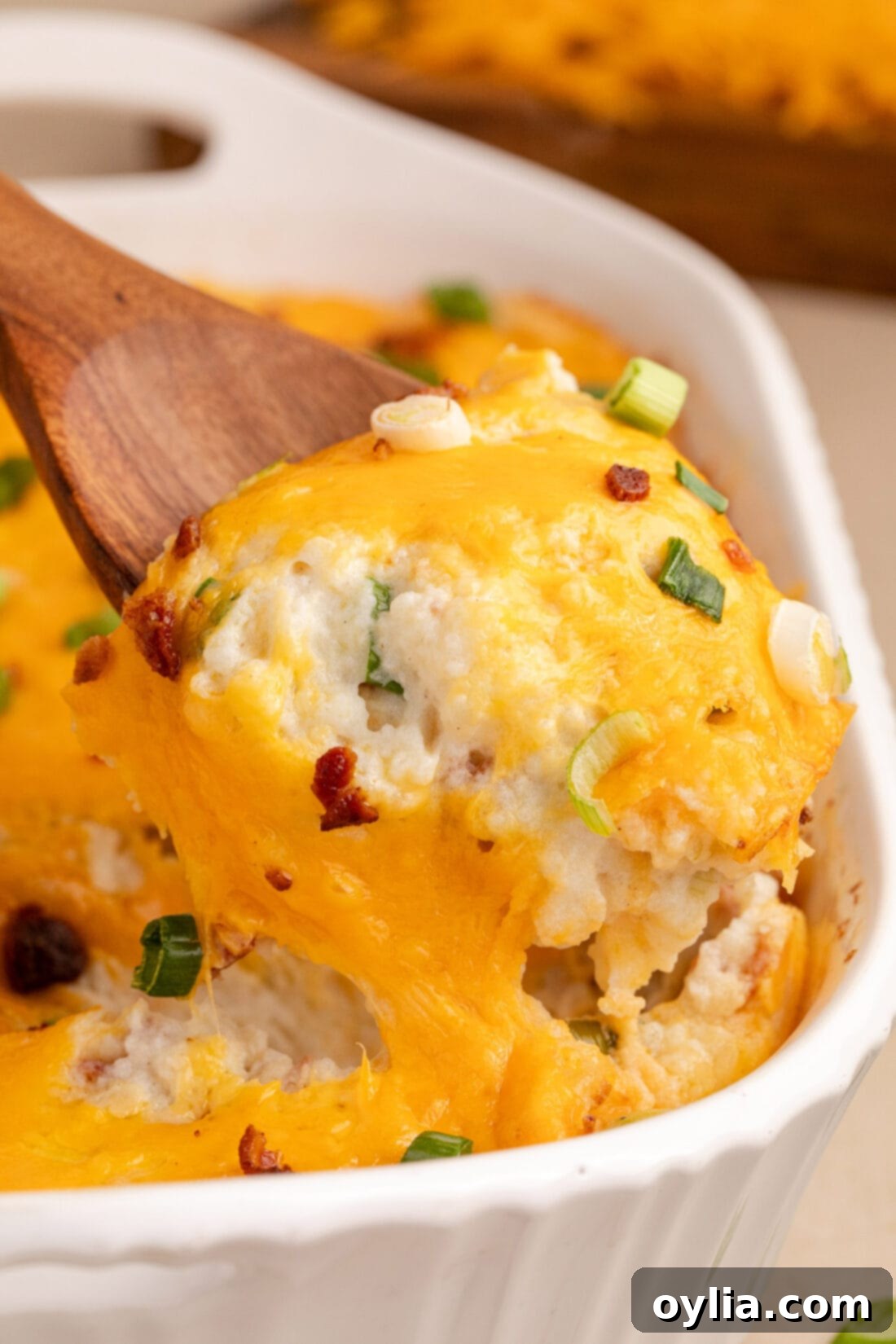 Ultimate Cheesy Potato Bake 2 Spoonful of Twice Baked Potato Casserole being lifted out of the casserole dish, showcasing creamy potatoes, bacon, and cheese.