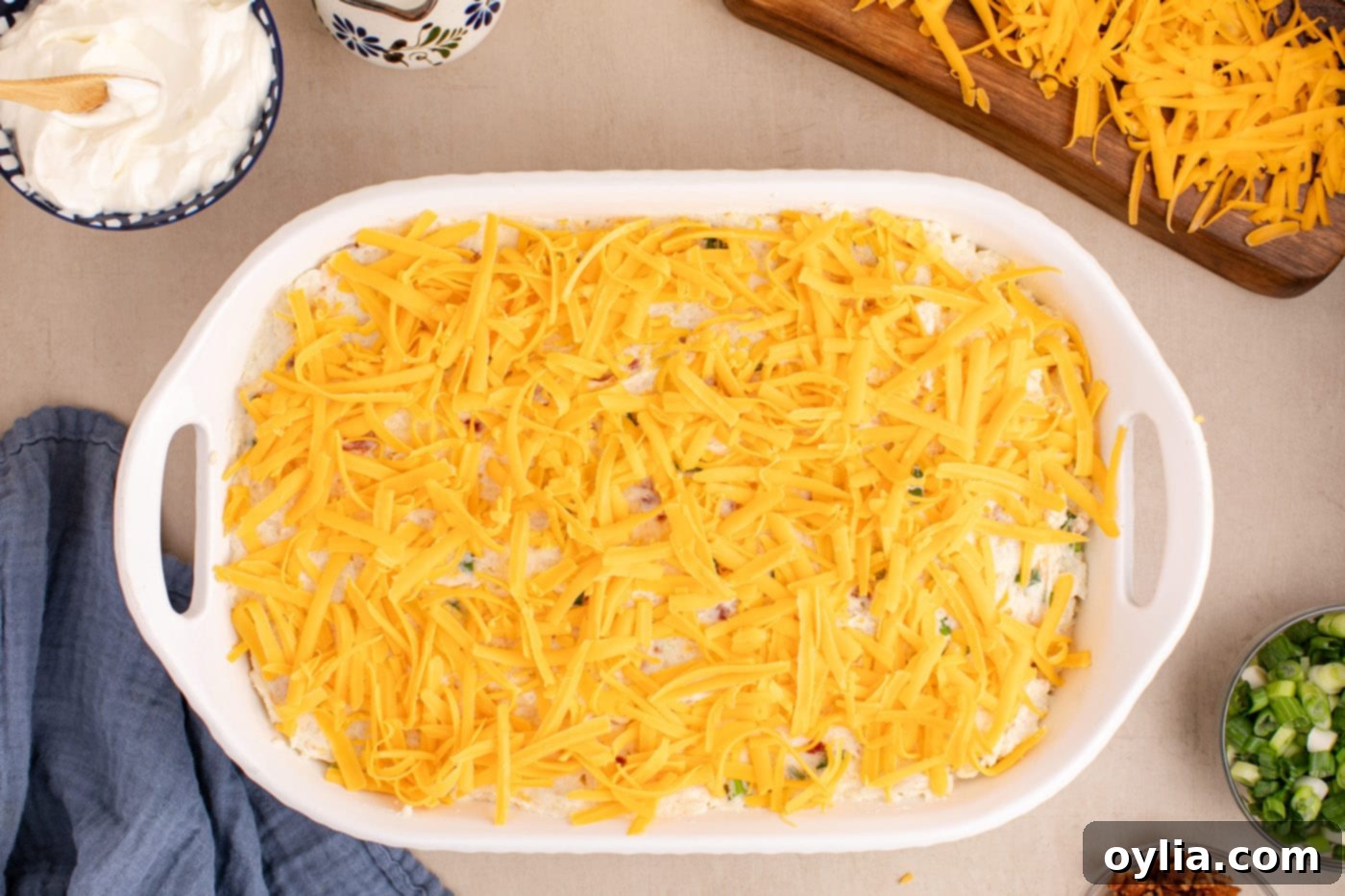 Shredded cheddar cheese generously sprinkled on top of the mashed potato casserole, ready for baking.