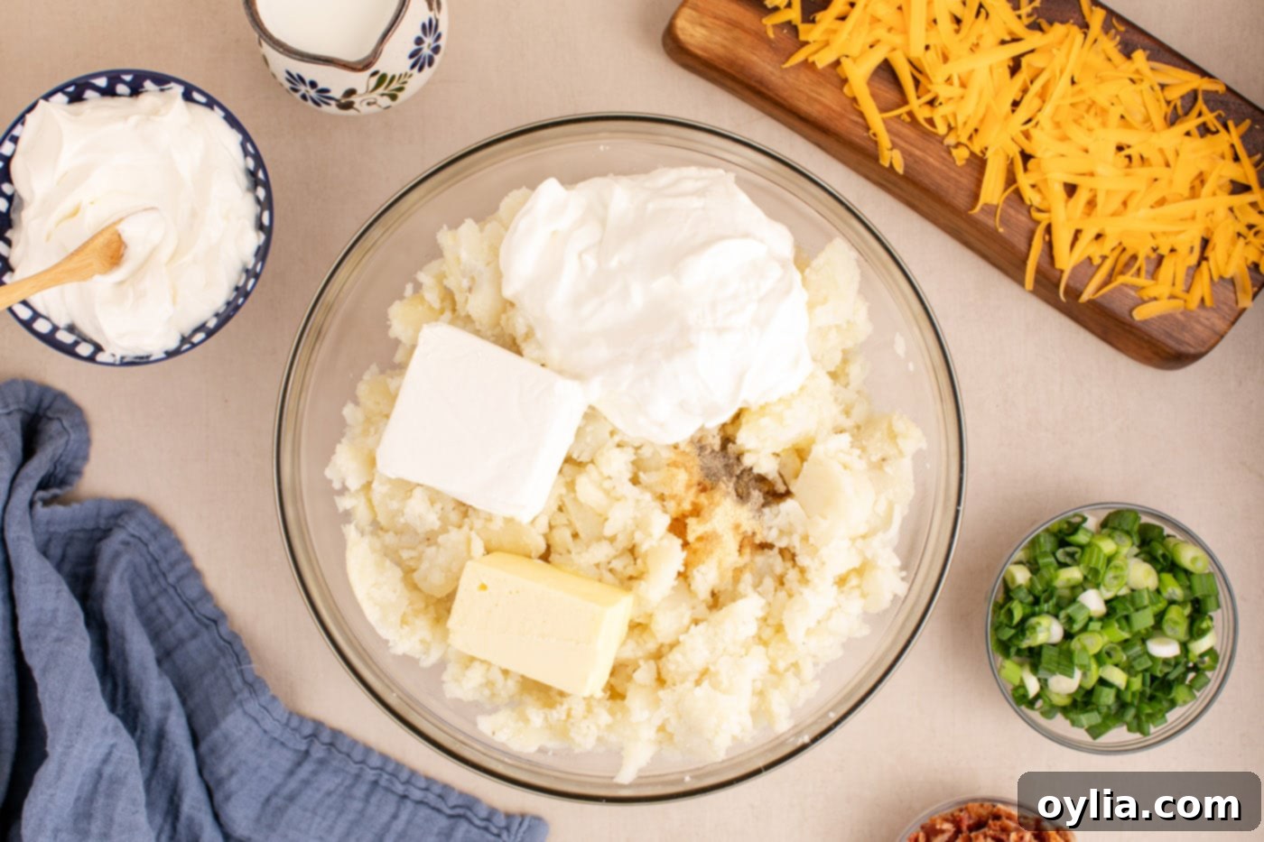 Sour cream, cream cheese, milk, butter, garlic powder, and ground pepper added to the mashed potatoes in a large mixing bowl.